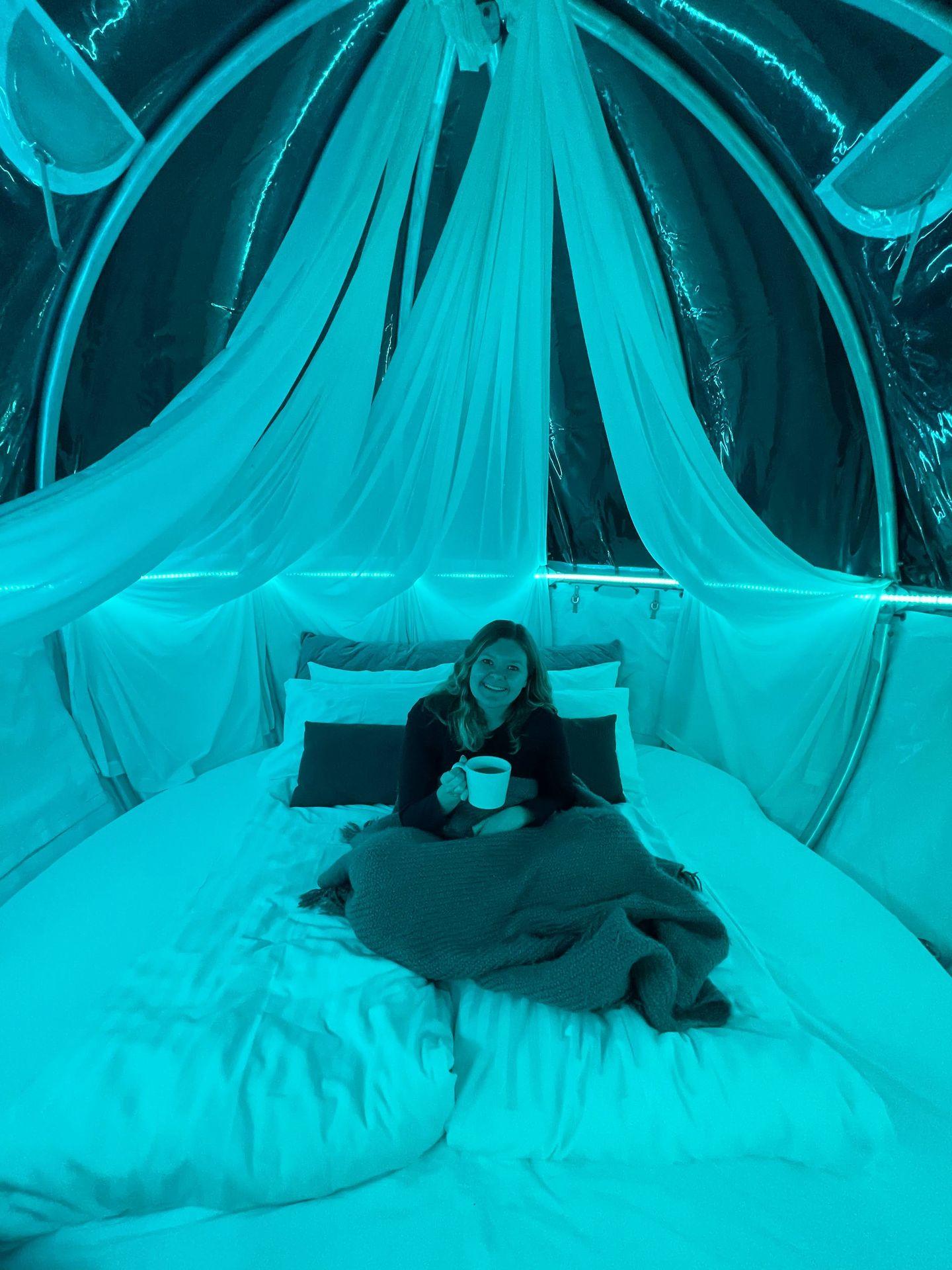 Lydia sitting inside of a clear bubble that is glowing blue. She holds a cup of coffee.