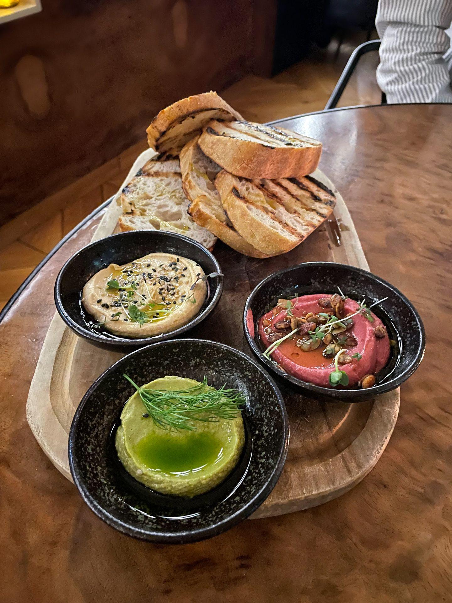 A tray with three colors of hummus and toasted bread.