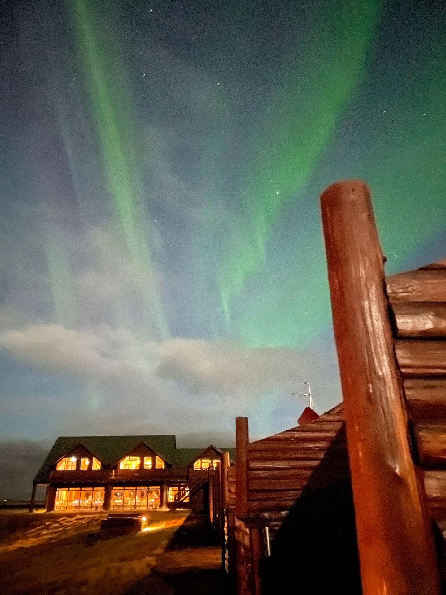 A wooden building with the Northern Lights above them.
