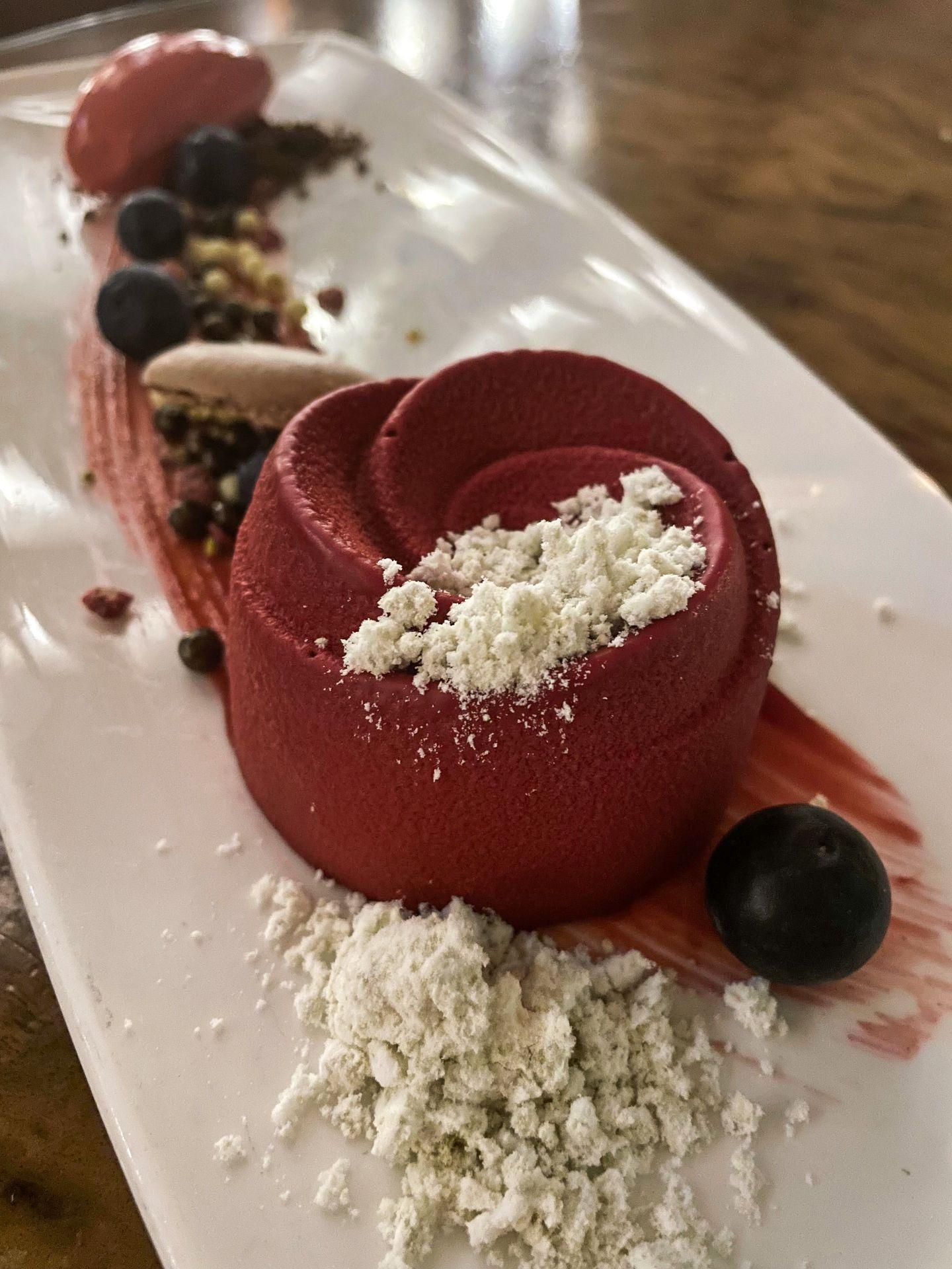 A dessert shaped like a red rose on a beautiful plate.