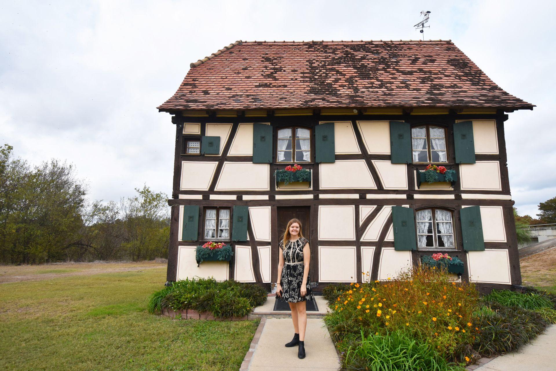 Lydia standing in front of the Alsatian Steinbach Haus, which is white with brown wood features.