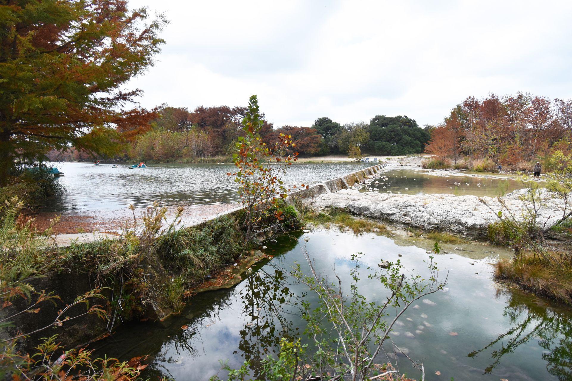 A view of the Frio River in Garner State Park in the fall. Trees with fall foliage surround the water.