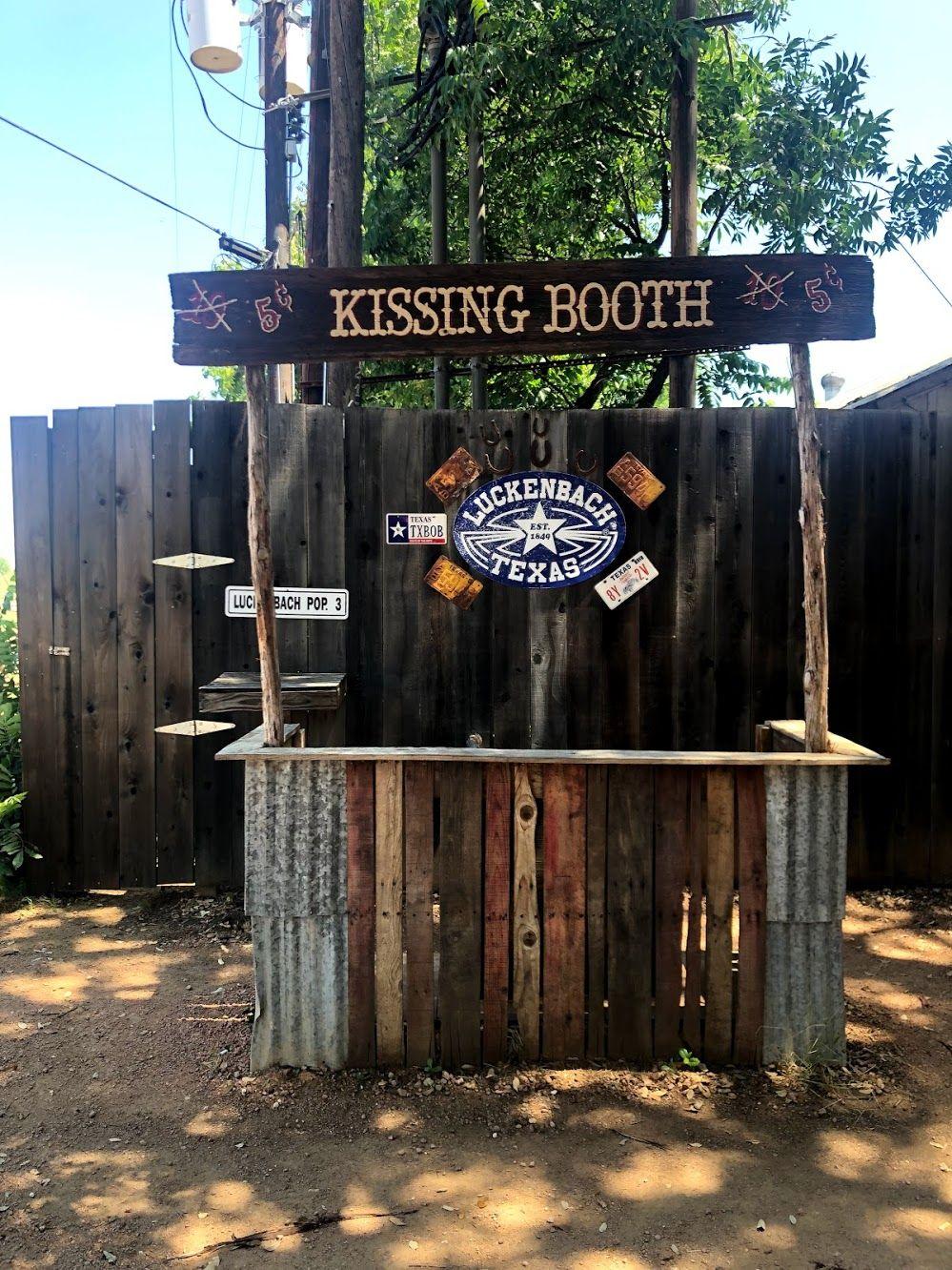 A wooden kissing booth with a Luckenbach sign on a fence behind it.