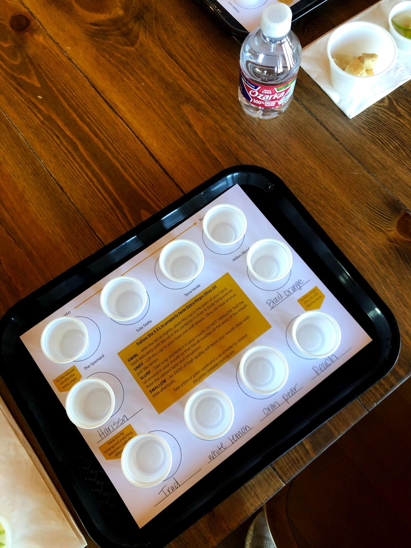 A tray of small plastic cups for olive oil and balsamic tastings. Each one is labeled and flavors include blood orange and white lemon.