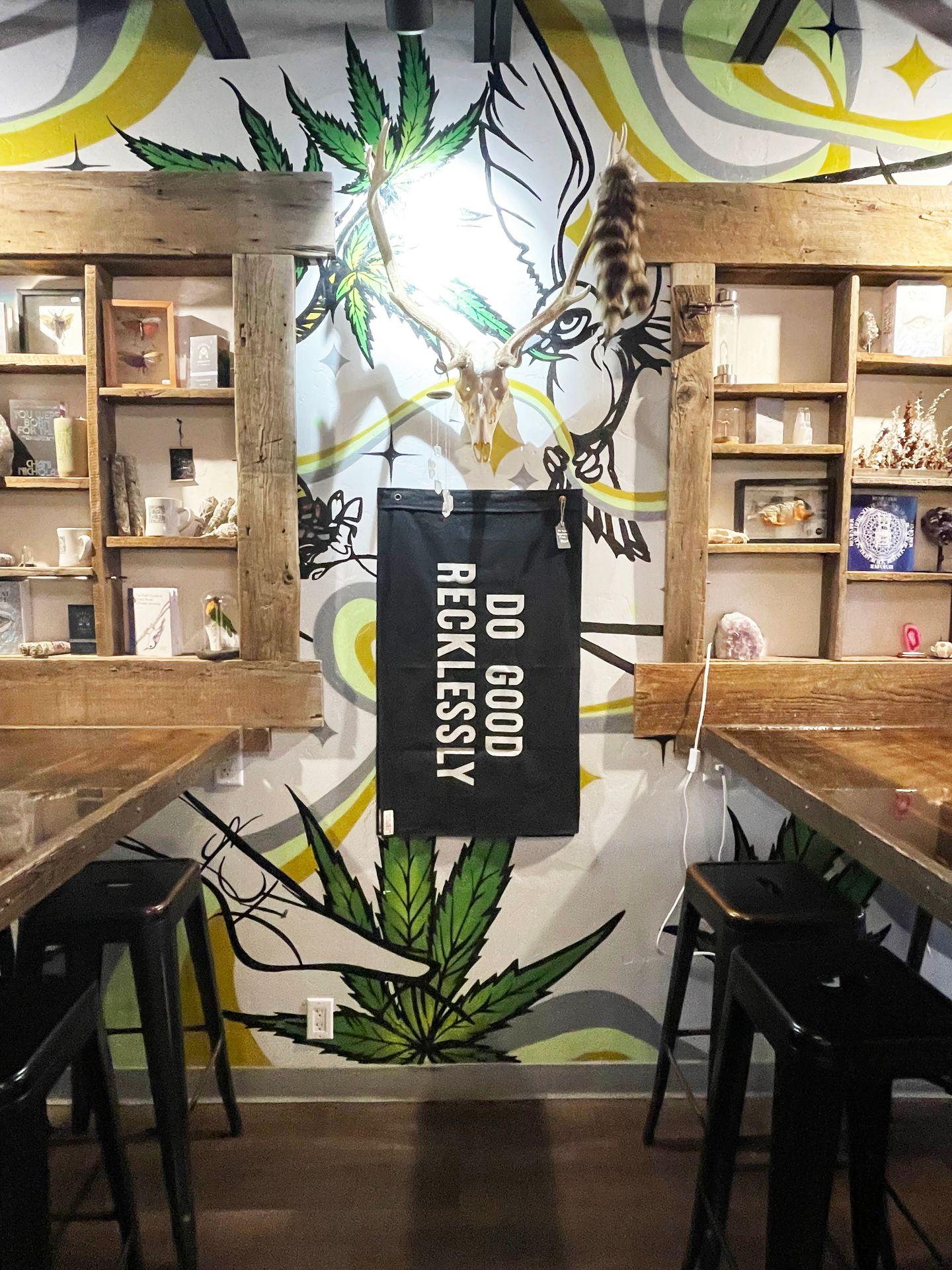Tables inside of House of Vibes. A sign reads "Do Recklessly Good" in the center and shelves with unique items sit behind the tables.