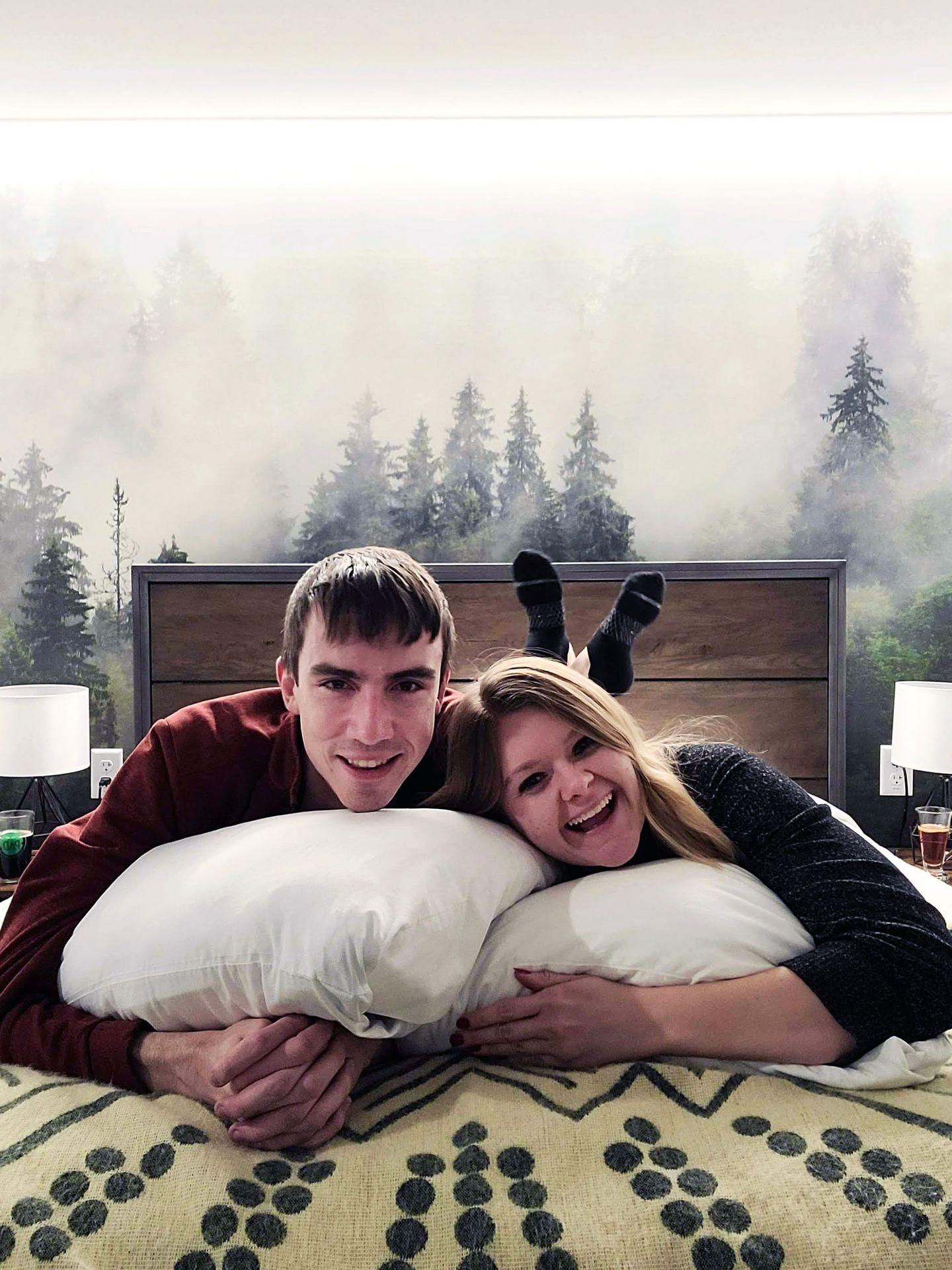 Lydia and Joe laying on their stomach on the bed in their room in The Pad. There is a beautiful scene of snowy trees in the background
