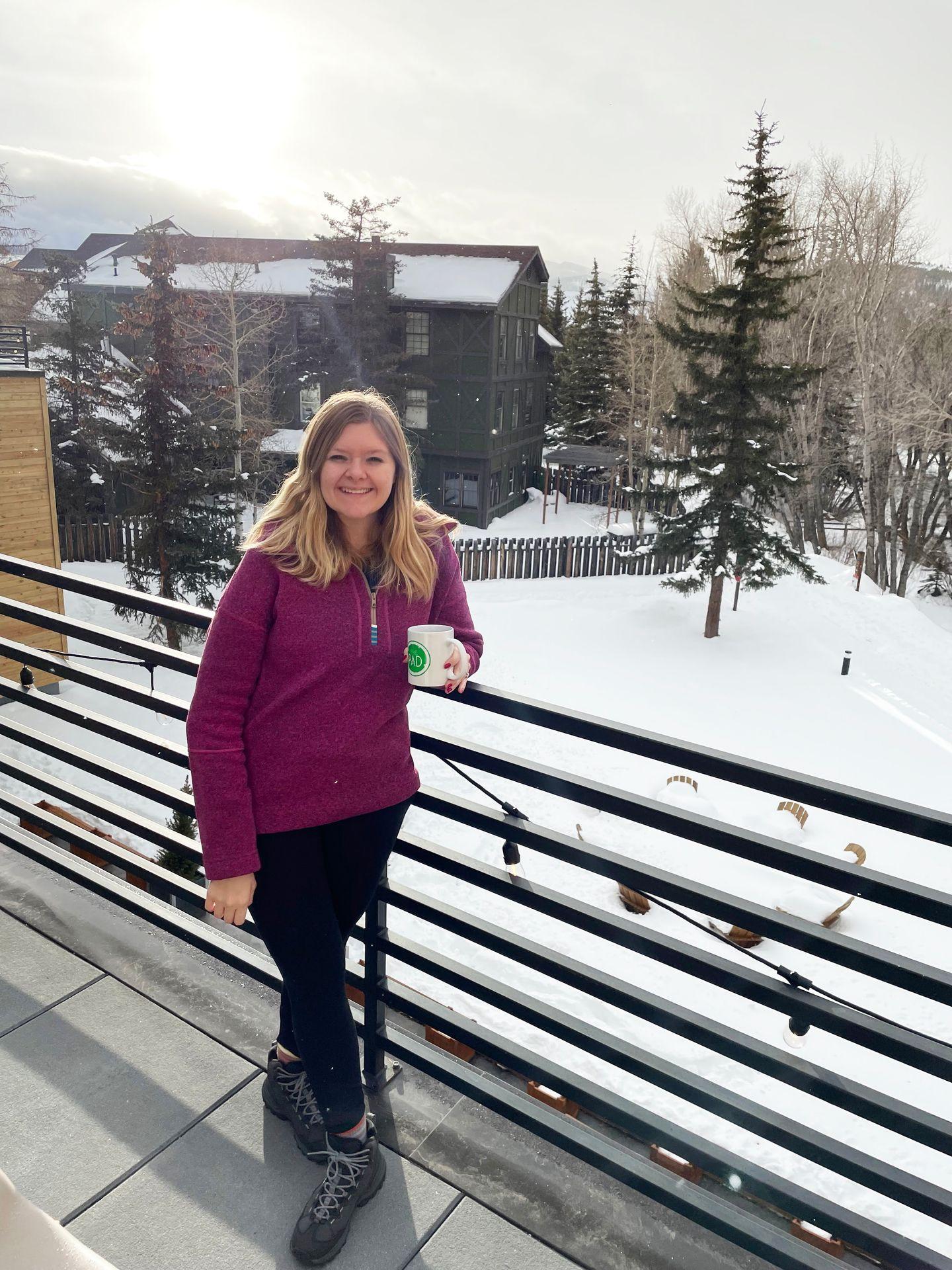 Lydia standing on the hot tub deck of The Pad holding a coffee mug, with snow on the ground in the background