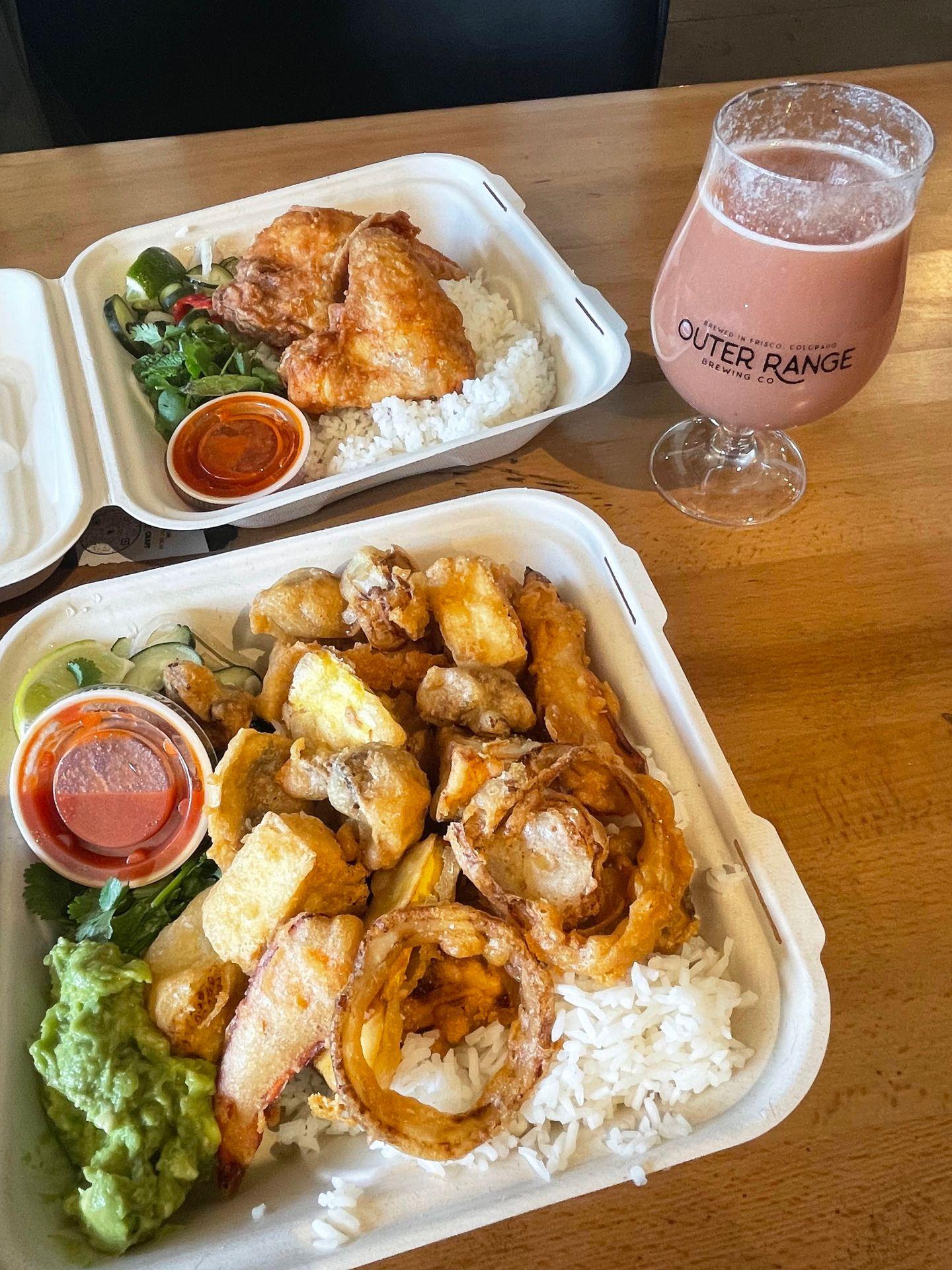 A table with two meals from Bird Craft and a smoothie sour beer. The closest meal is the tofu and veggie bowl, which includes white rice, fried vegtables, tofu, guacamole and a red sauce in a cup.