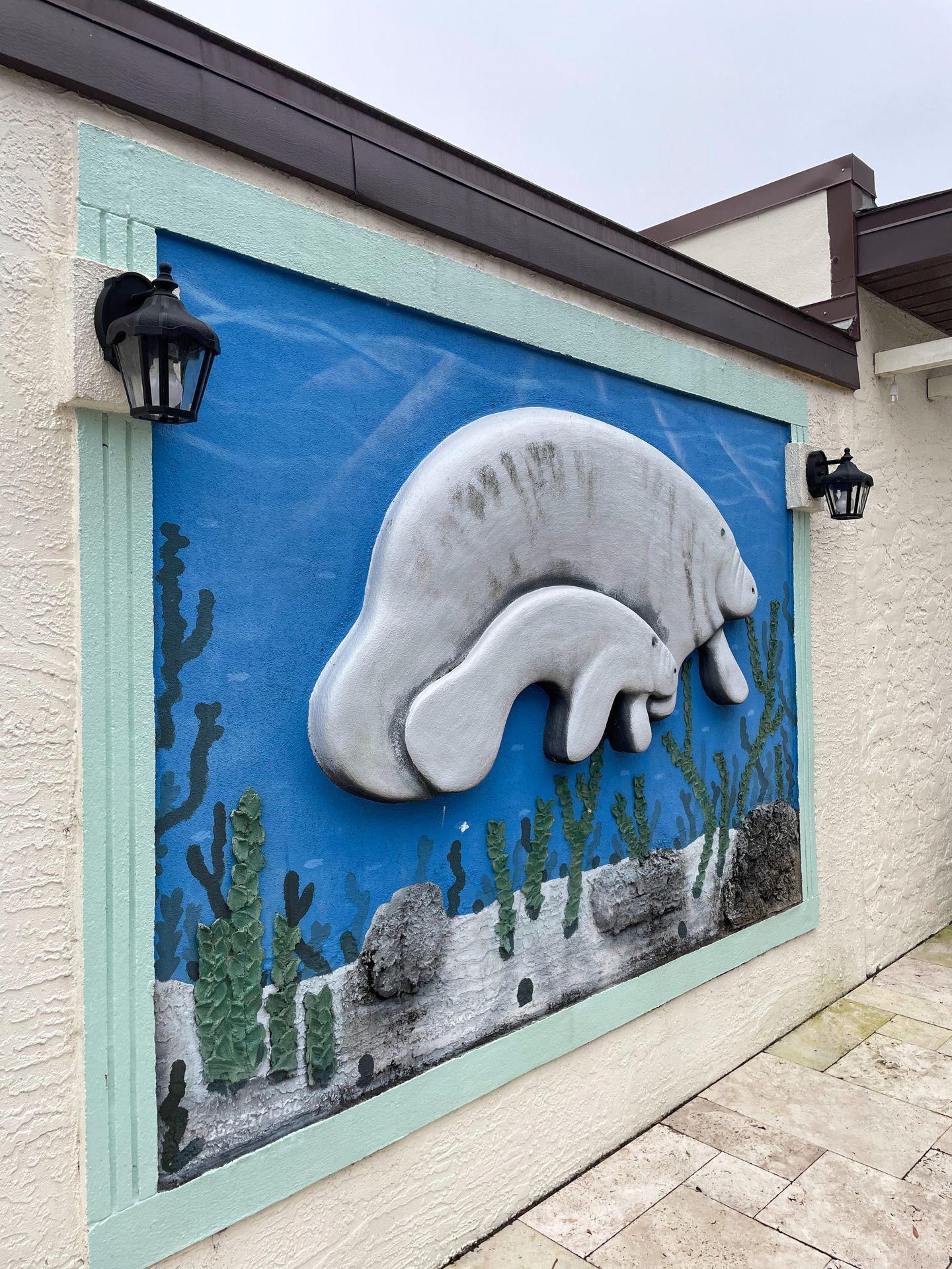 A piece of artwork with mantees swimming. It is on the wall outside at the Retreat of Crystal Manatee.