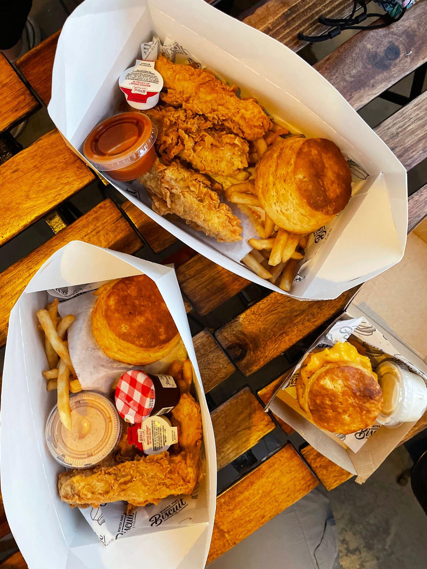 Some paper baskets with fried chicken, biscuits, french fries and sauces.