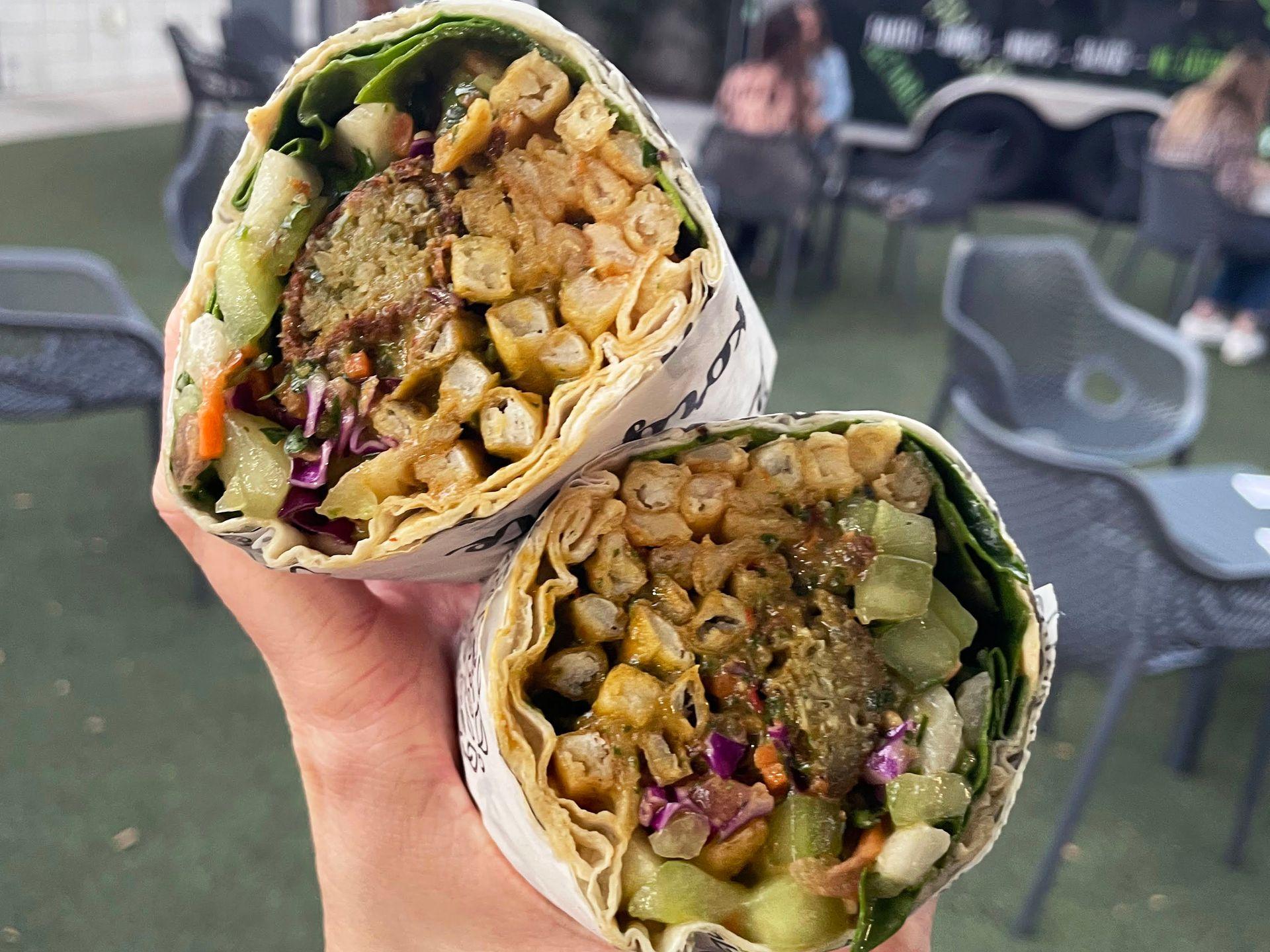 A close up of a burrito cut in half. Inside there is falafel, french fries and veggies.