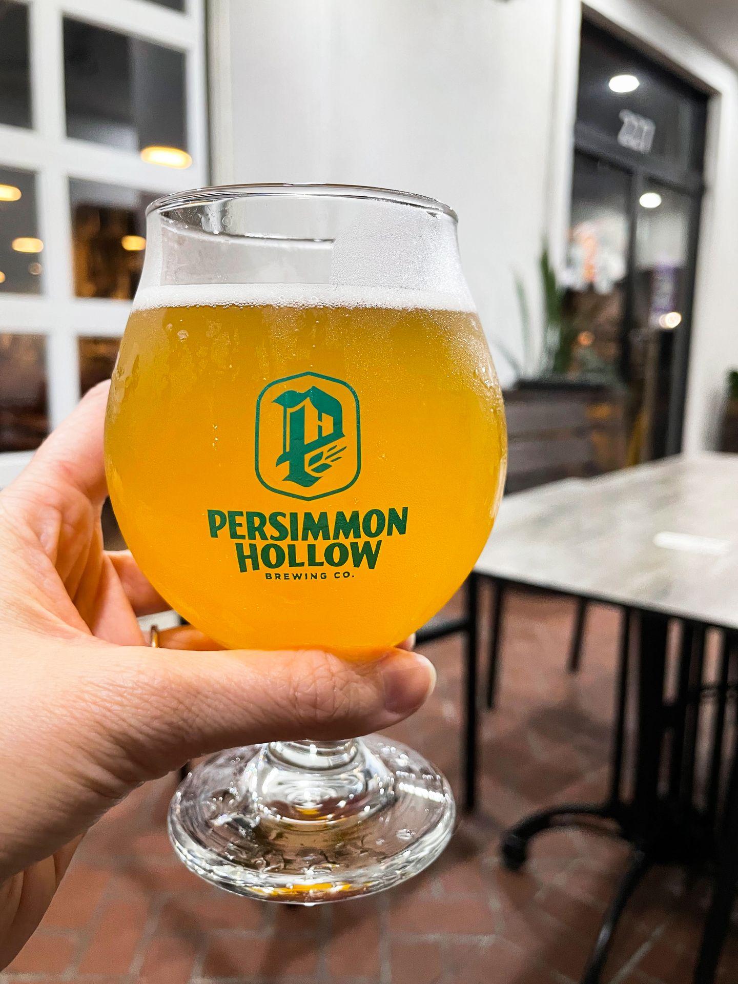 Holding up a golden beer in a glass that reads 'Persimmon Hollow.'