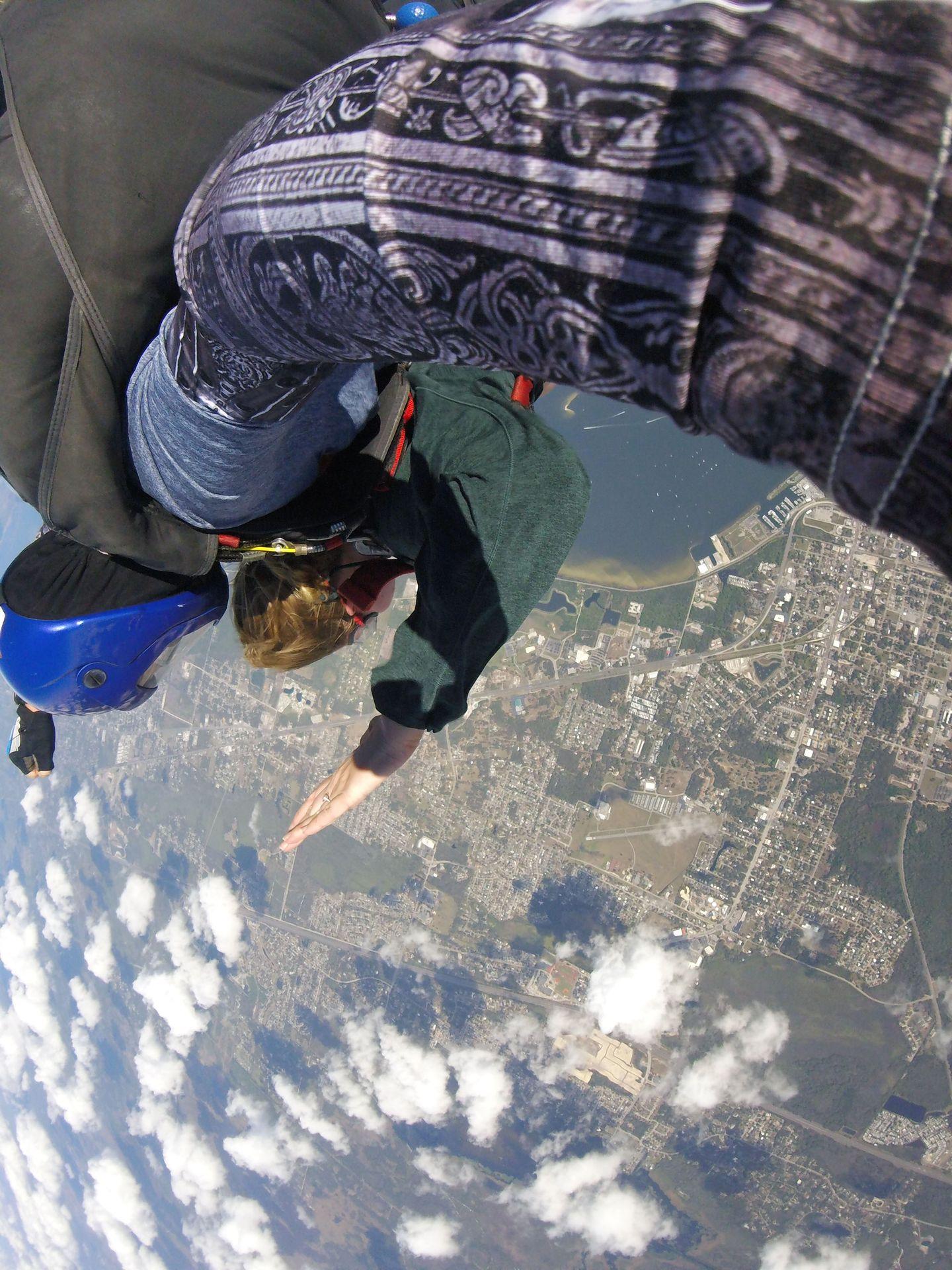 A photo of Lydia skydiving. There are clouds and land below.