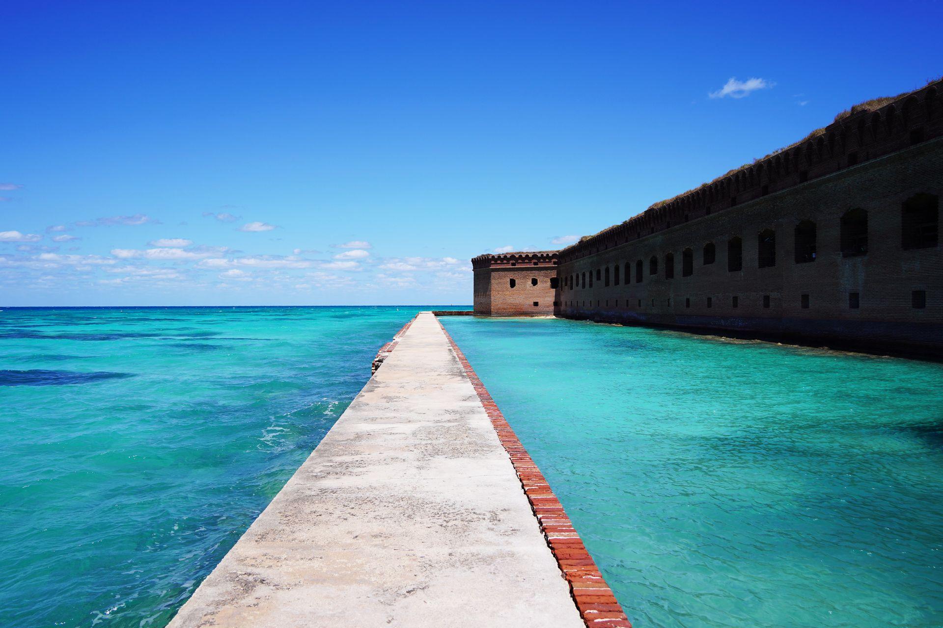 A narrow path surrounding by water on both sides with an old military fort in the background at Dry Tortugas National Park