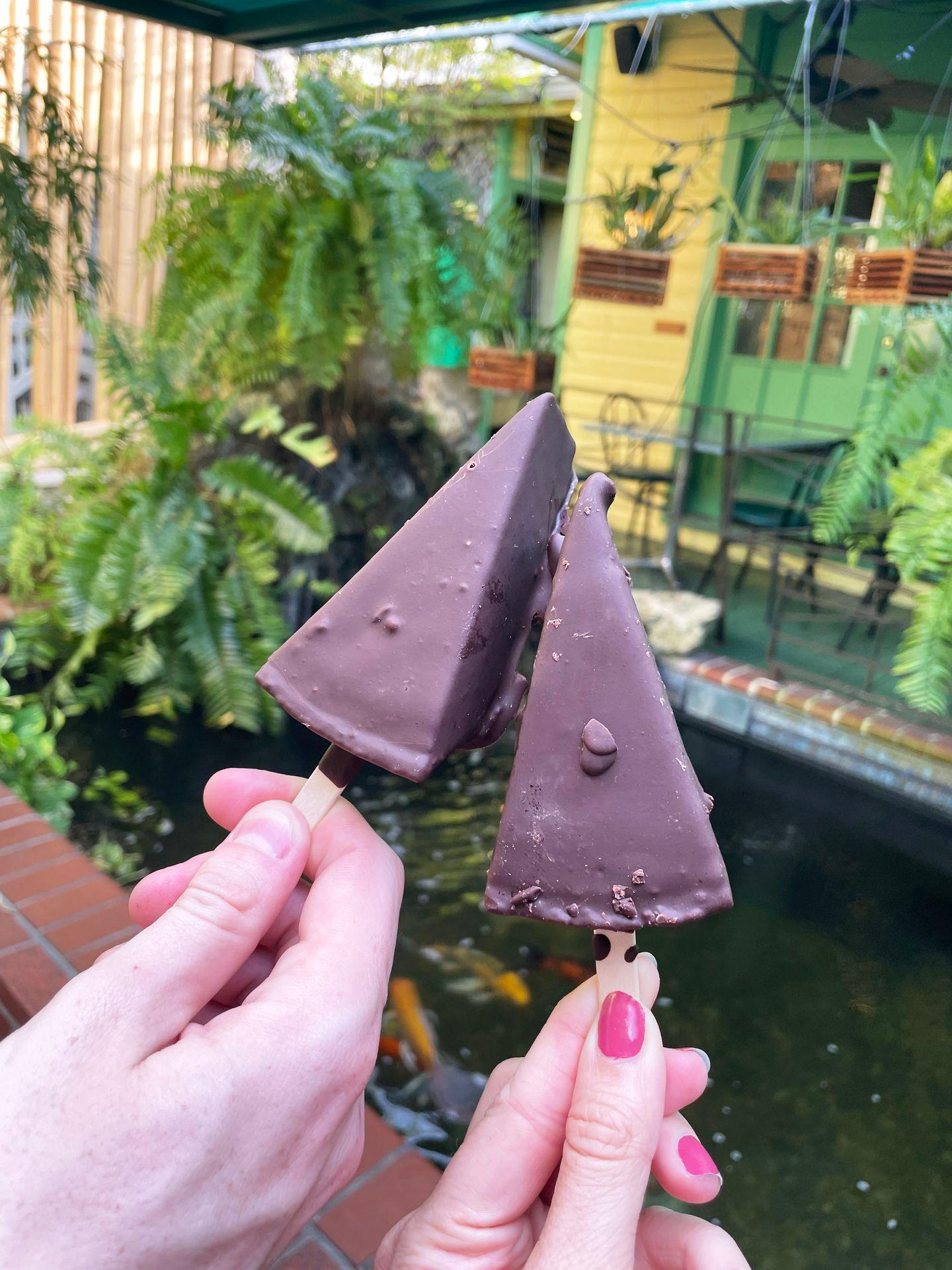 Two chocolate covered key lime pies on a stick being held up