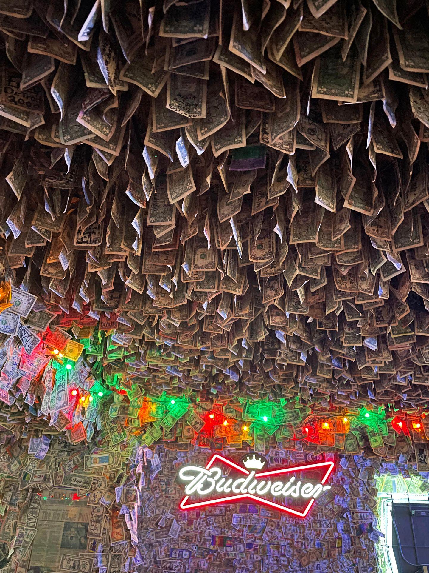Dollar bills covering the ceiling and walls with a Budweiser neon sign and red and green string lights