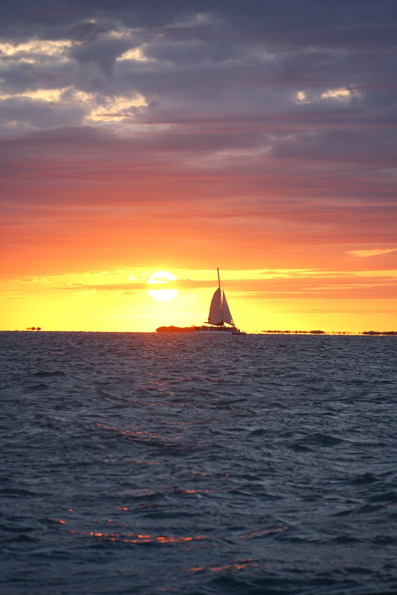 The sunset over the ocean with a sailboat silhouetting the sky