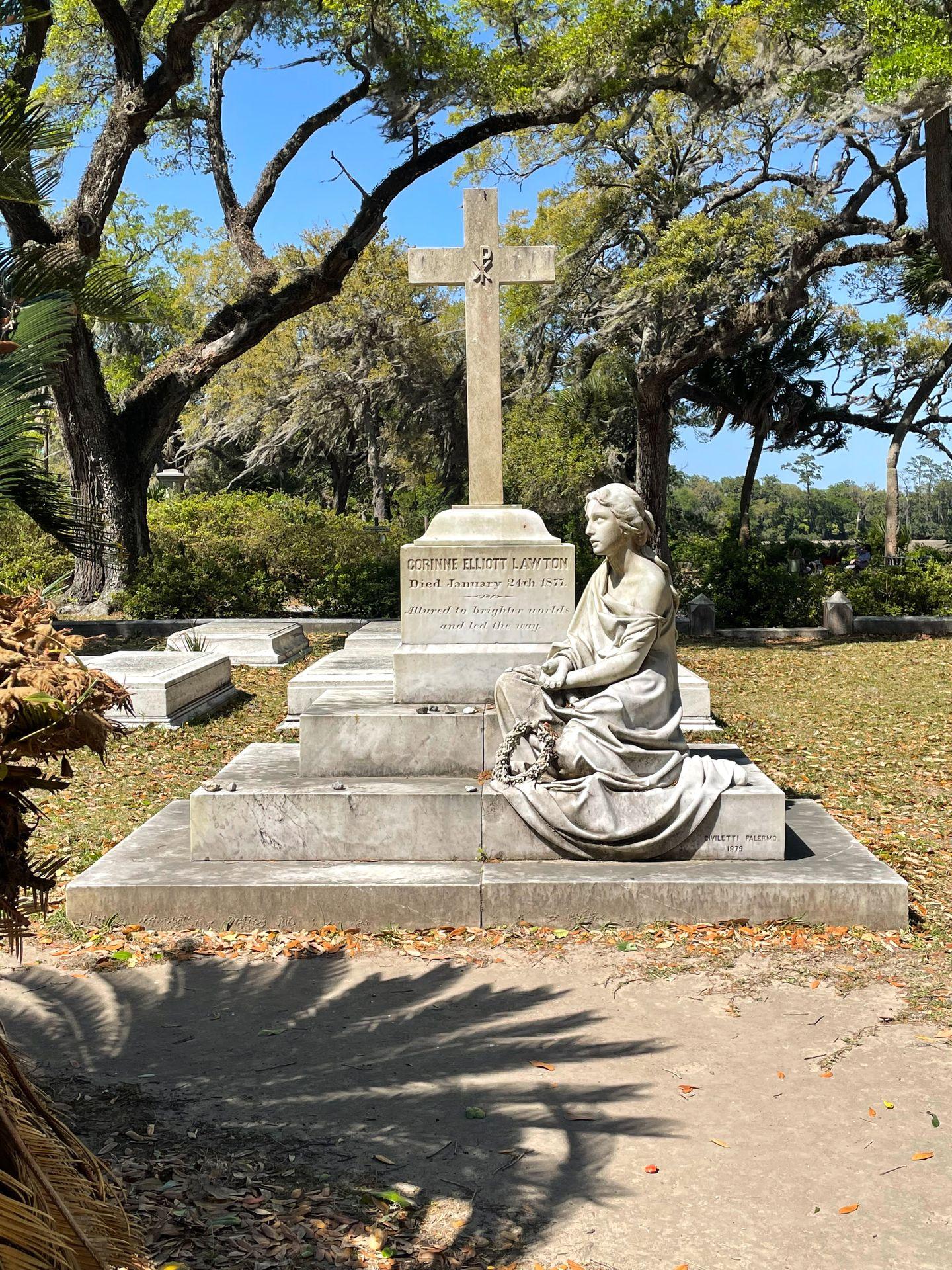 A cross with a person sitting next to it at Bonaventure Cemetery