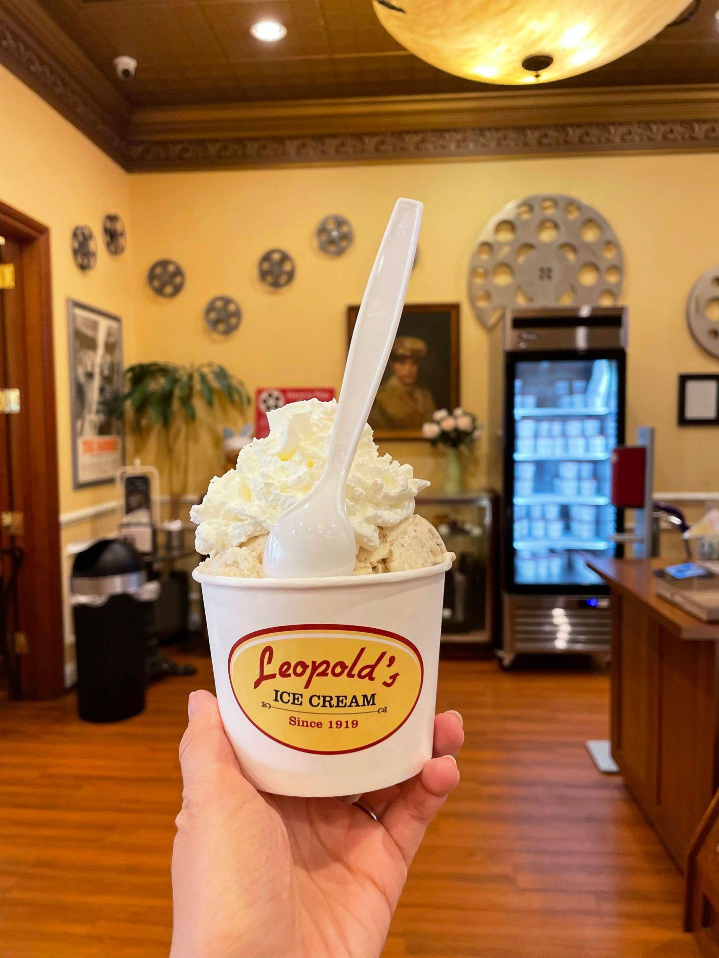 Holding up a cup of ice cream topped with whipped cream inside of Leopold's Ice Cream