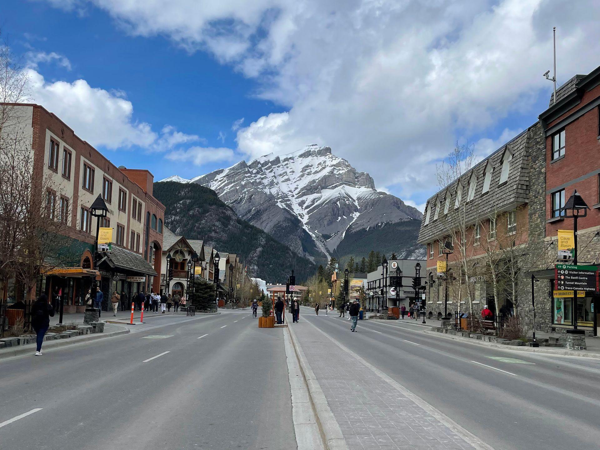 The main street of downtown Banff. There are shops and restaurants on either side a large mountain in the center.