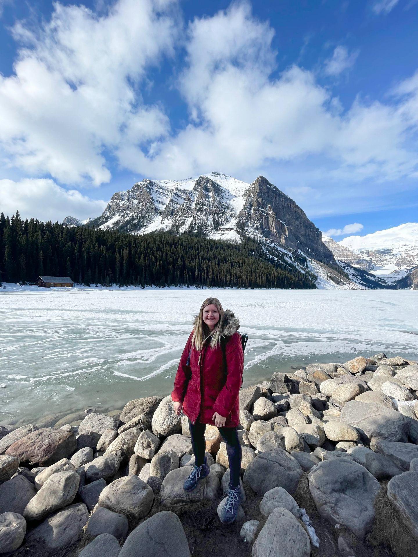 Lydia standing in front of a frozen lake. There are large mountains across the lake.