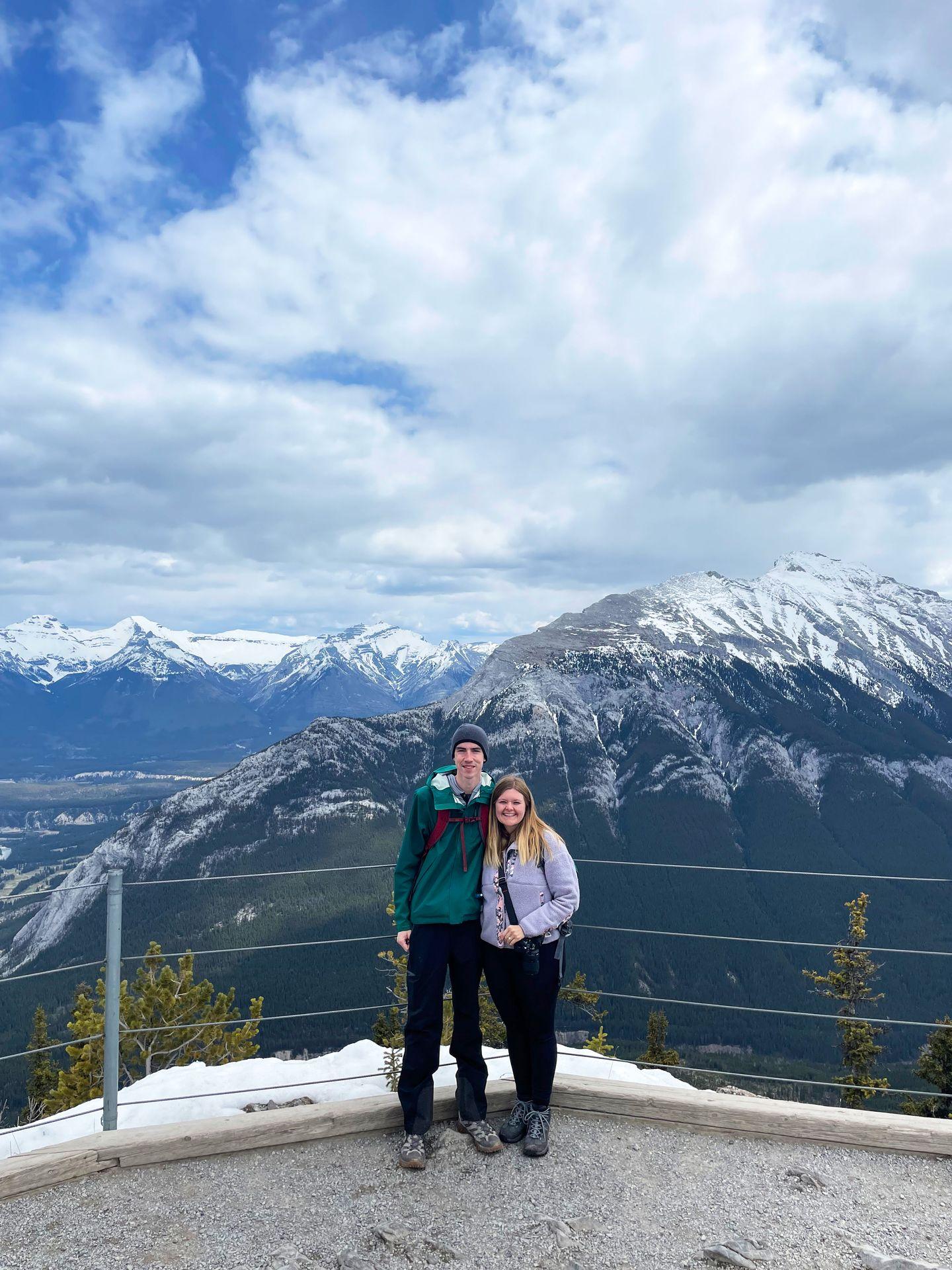 Lydia and Joe standing on the top of Sulphur Mountain with a view of mountains in the distance.