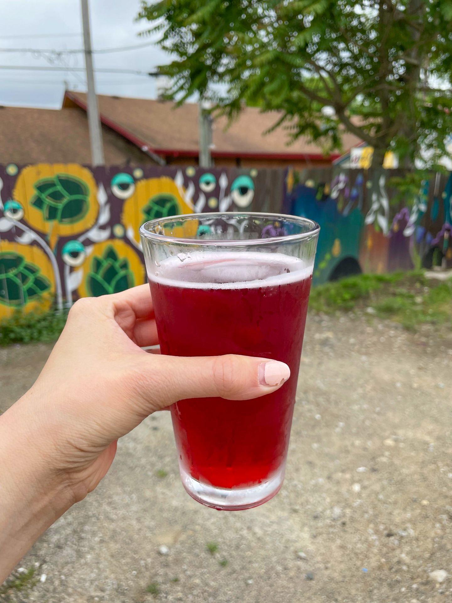 Holding up a beer on the patio of Trail Town Brewing. The background is a colorful fence painted with murals.