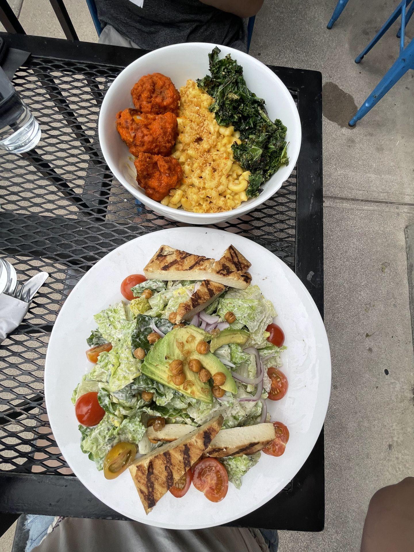 A plate of a vegan caesar salad and a plate with mac and cheese, green and buffalo faux chicken at Tasty Harmony, a vegetarian restaurant in Fort Collins.