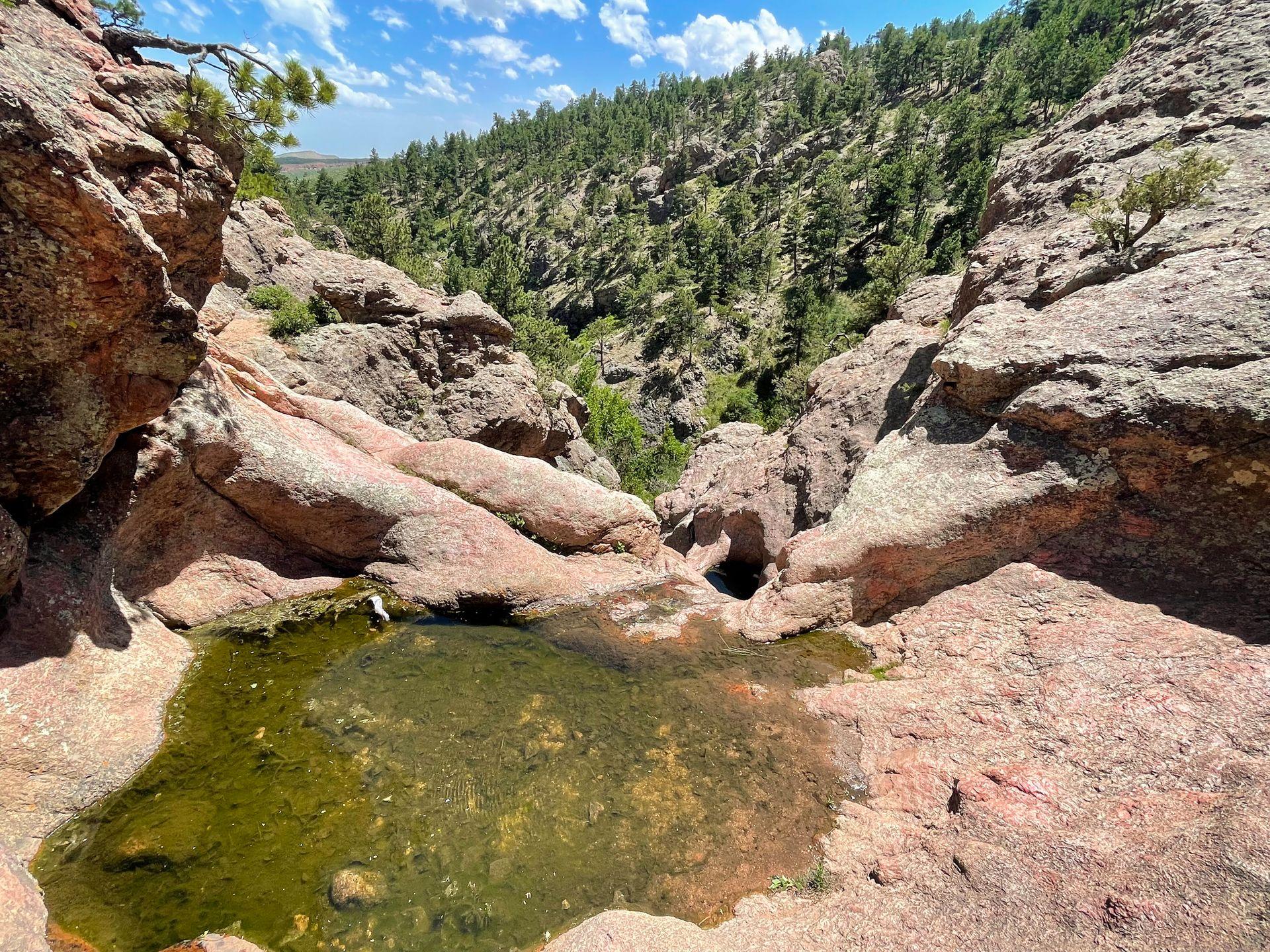 An area of red rocks with a pool of green water on the Horsetooth Falls Trail near Fort Collins.