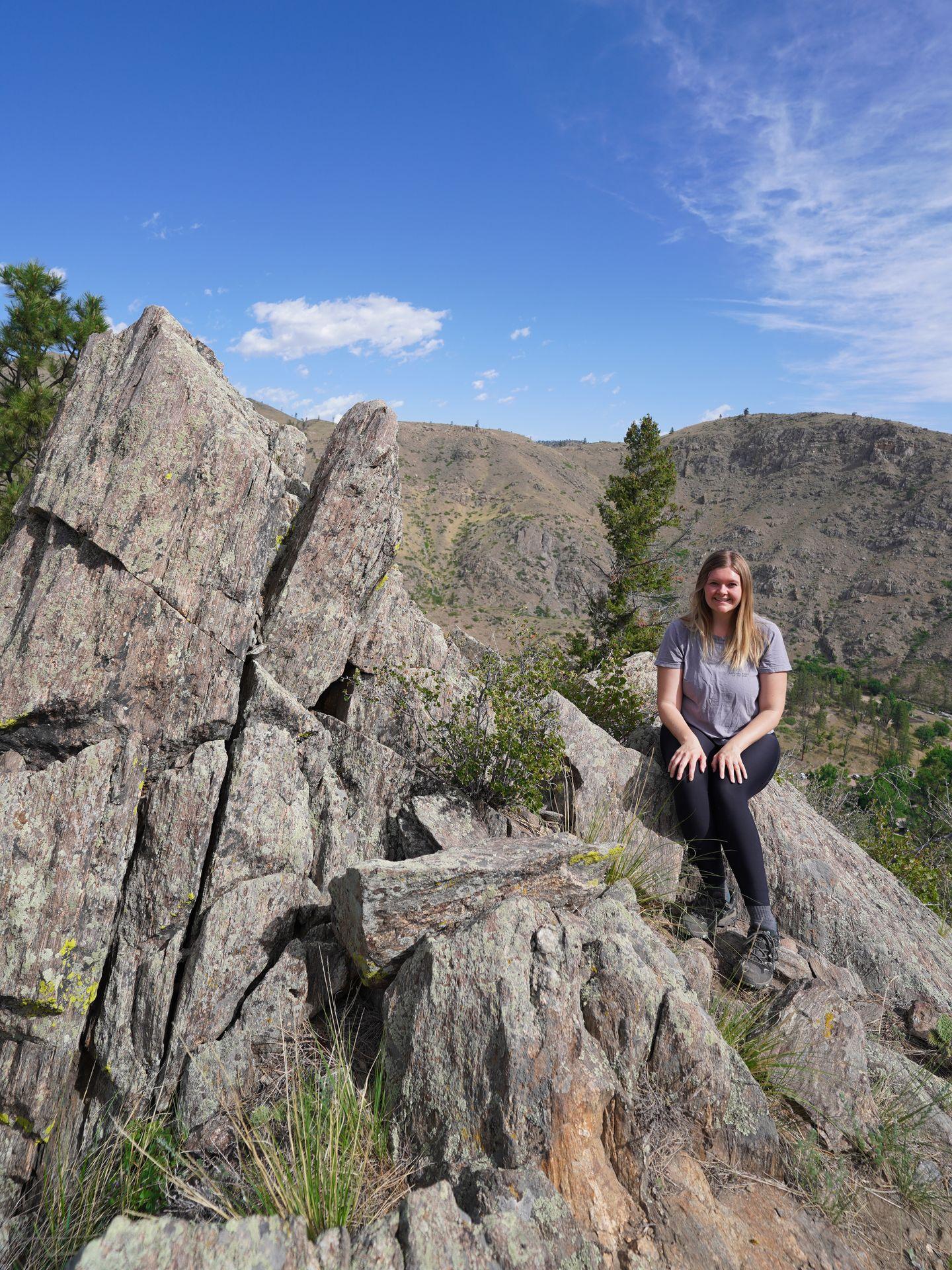 Lydia sitting on an area of black, jagged rocks along the Black Powder Trail in the Gateway Natural Area.