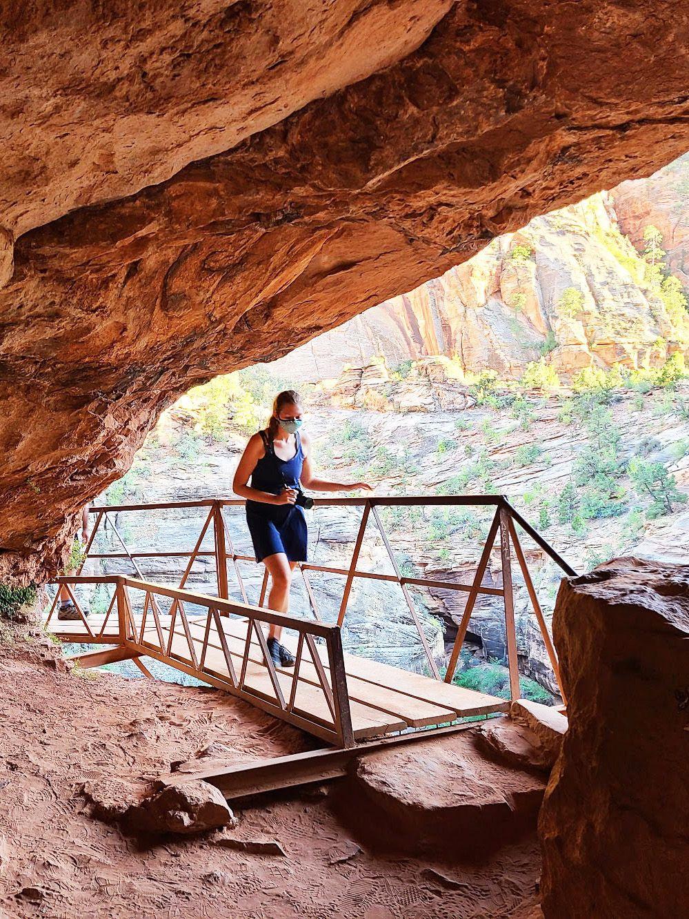 Lydia hiking on a wooden bridge under a rock overhang on the Canyon Overlook Trail in Zion National Park.