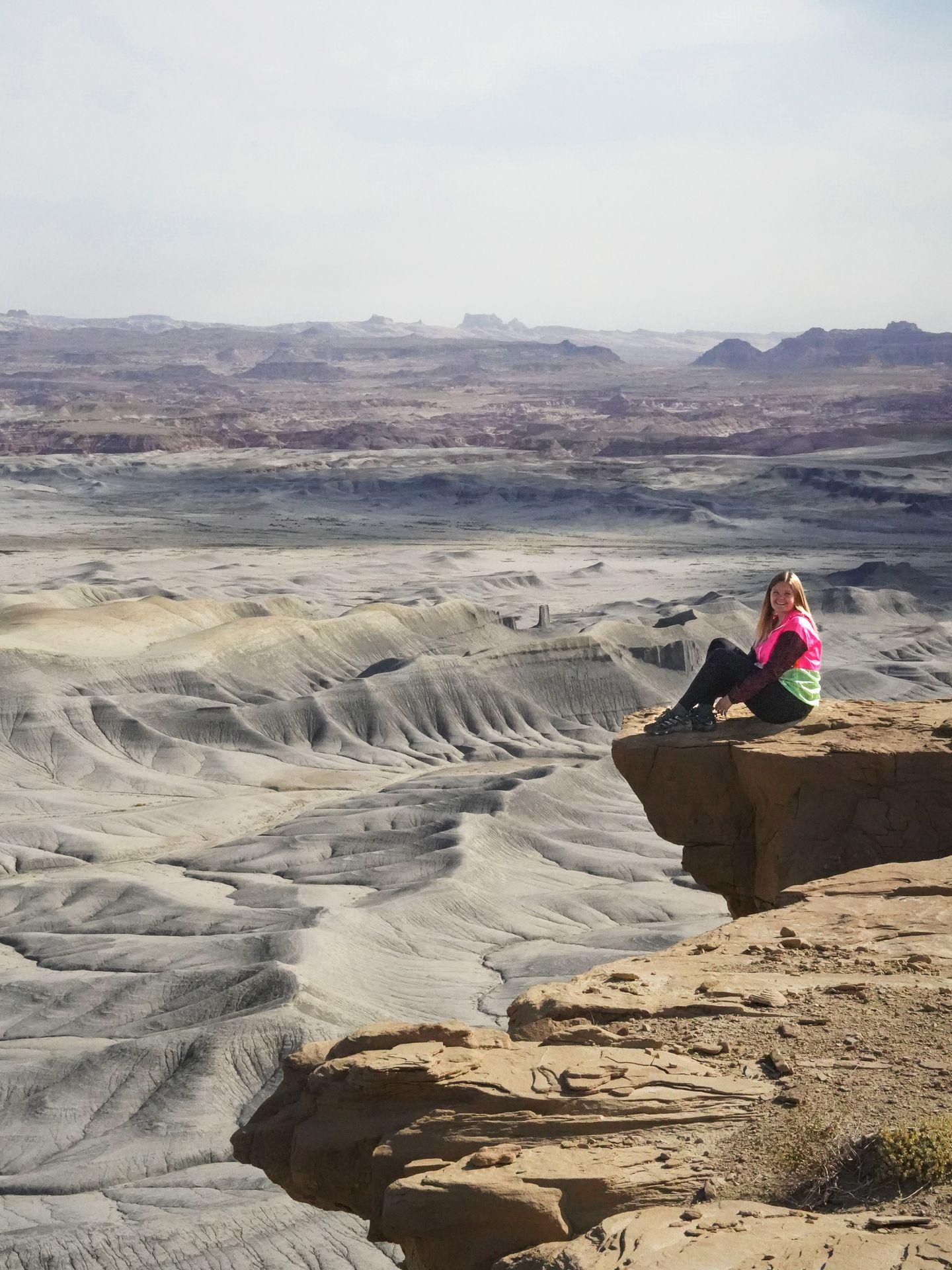 Lydia sitting on the edge of a rock with a view of a gray canyon in the distance at the Moonscape Overlook.