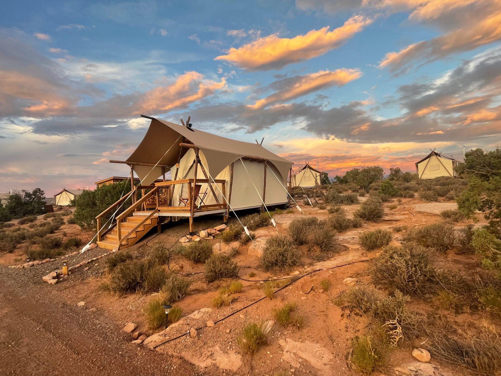 An area with several safari tents at Under Canvas Moab. The sky is colorful at sunset.