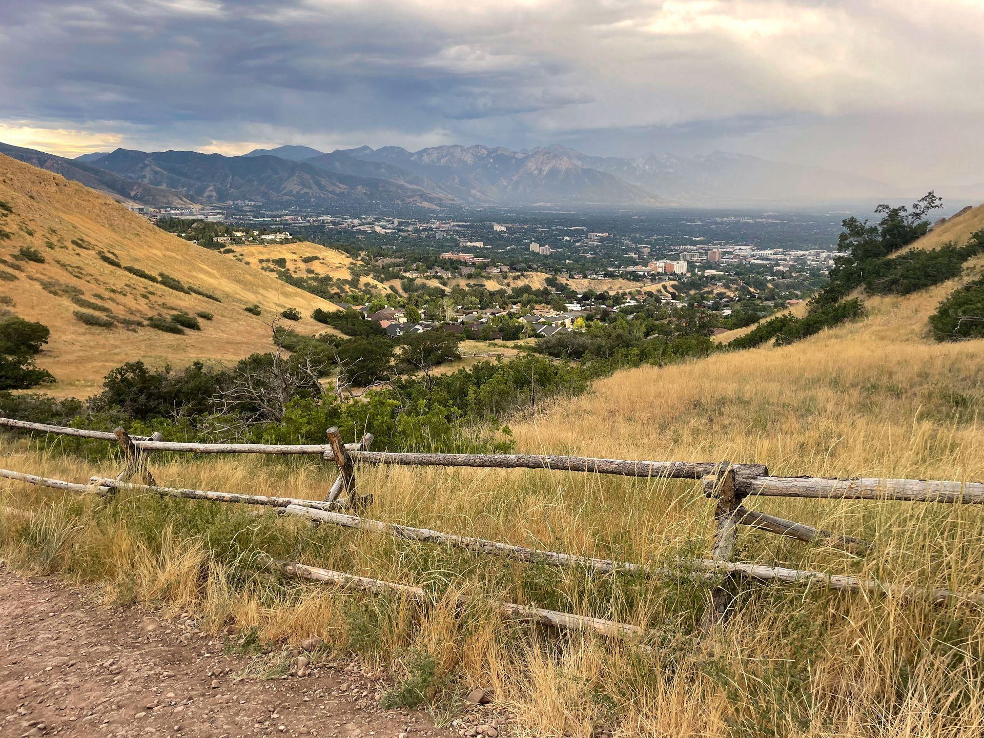 A view from the Ensign Peak trail with yellow hillsides, a city and mountains in the distance.