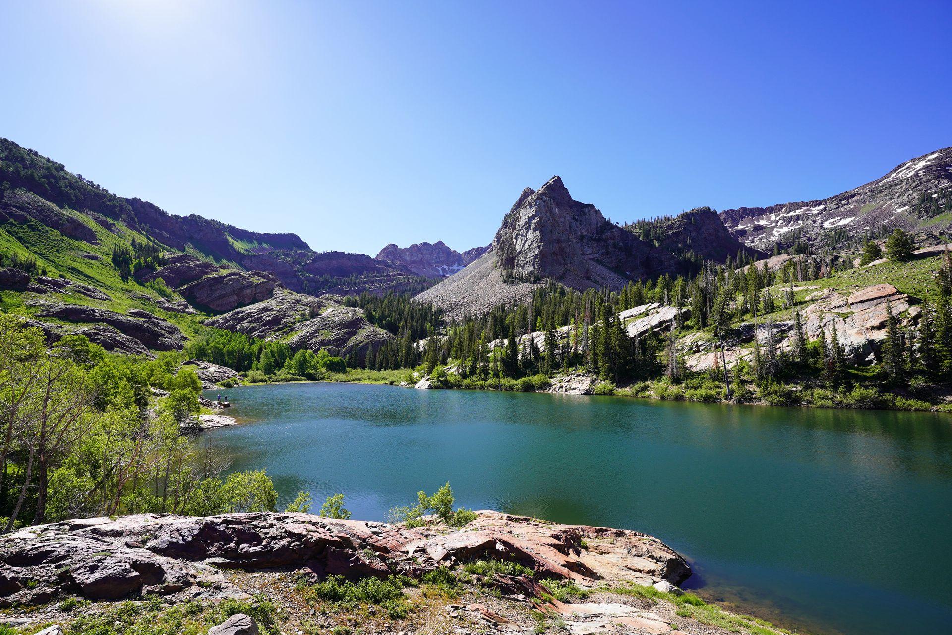 A view of Lake Blanche with a mountain on the opposite side of the lake. The lake is surrounded by rock and green trees.