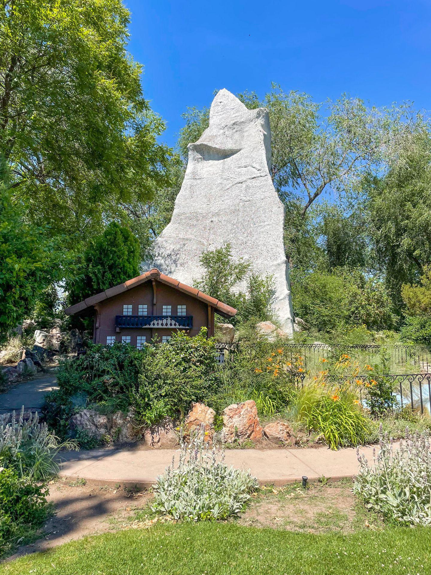 A large rock behind a house, representing Switzerland at the International Peace Gardens in Salt Lake City.
