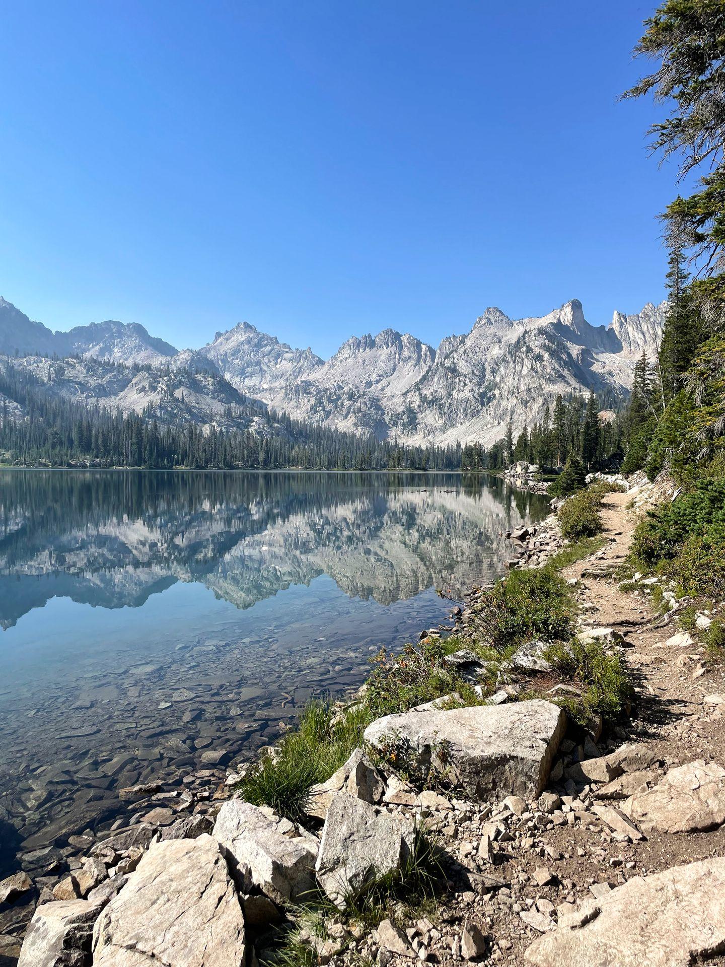 A view of Alice Lake with mountains reflecting in the water. A trail follows along the edge of the water.