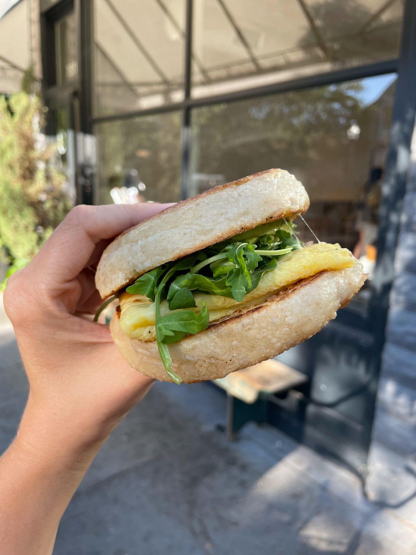 Holding up a breakfast sandwich on an english muffin from Certified Kitchen and Bakery.