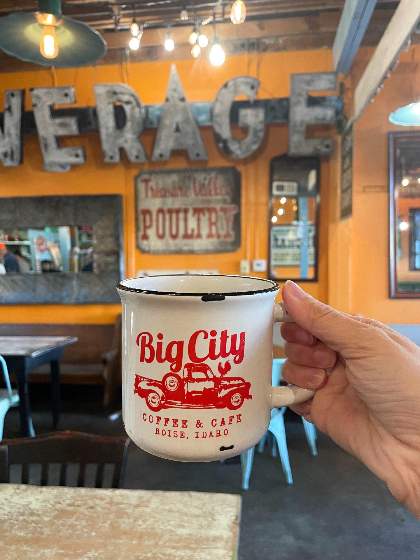 Holding up a white coffee mug that reads "Big City Coffee & Cafe, Boise, Idaho" in red letters.