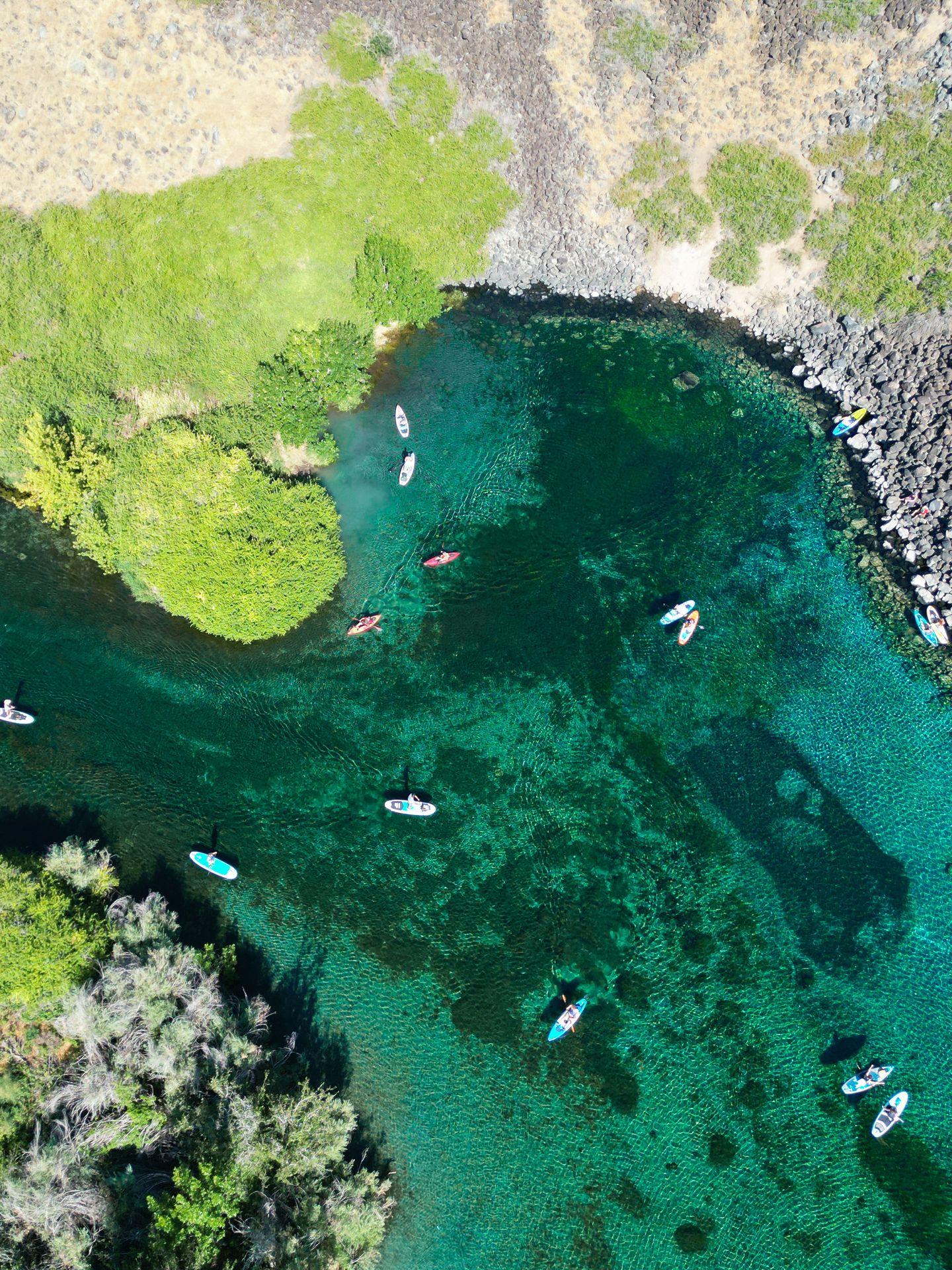 A drone shot of the heart-shaped Blue Heart Springs with several kayaks and paddle boards in the water.