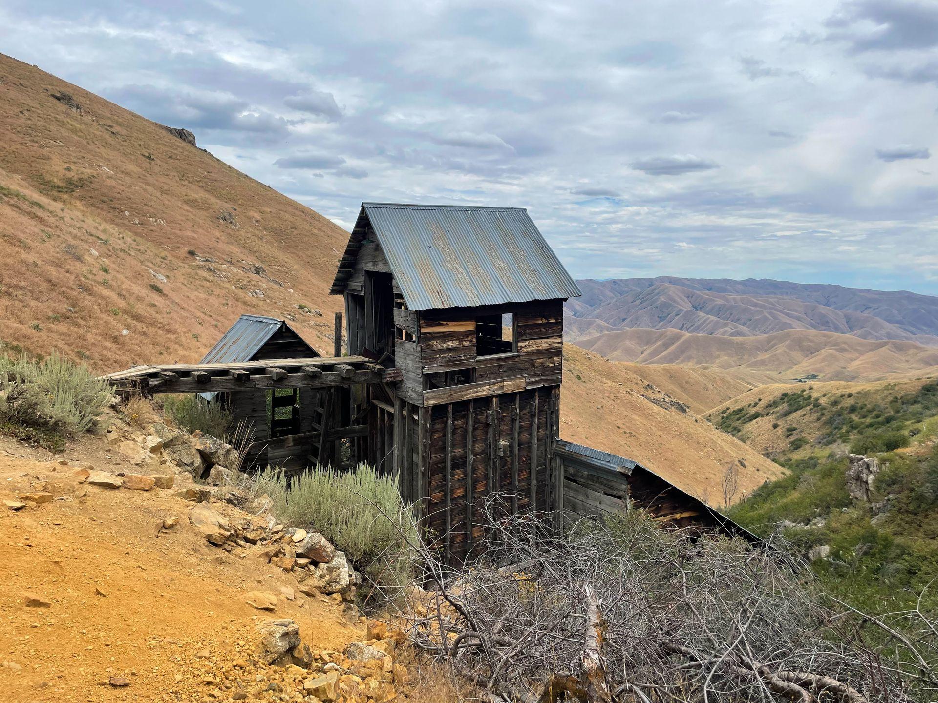A wood mine building perched on a hill with rolling hills in the distance.