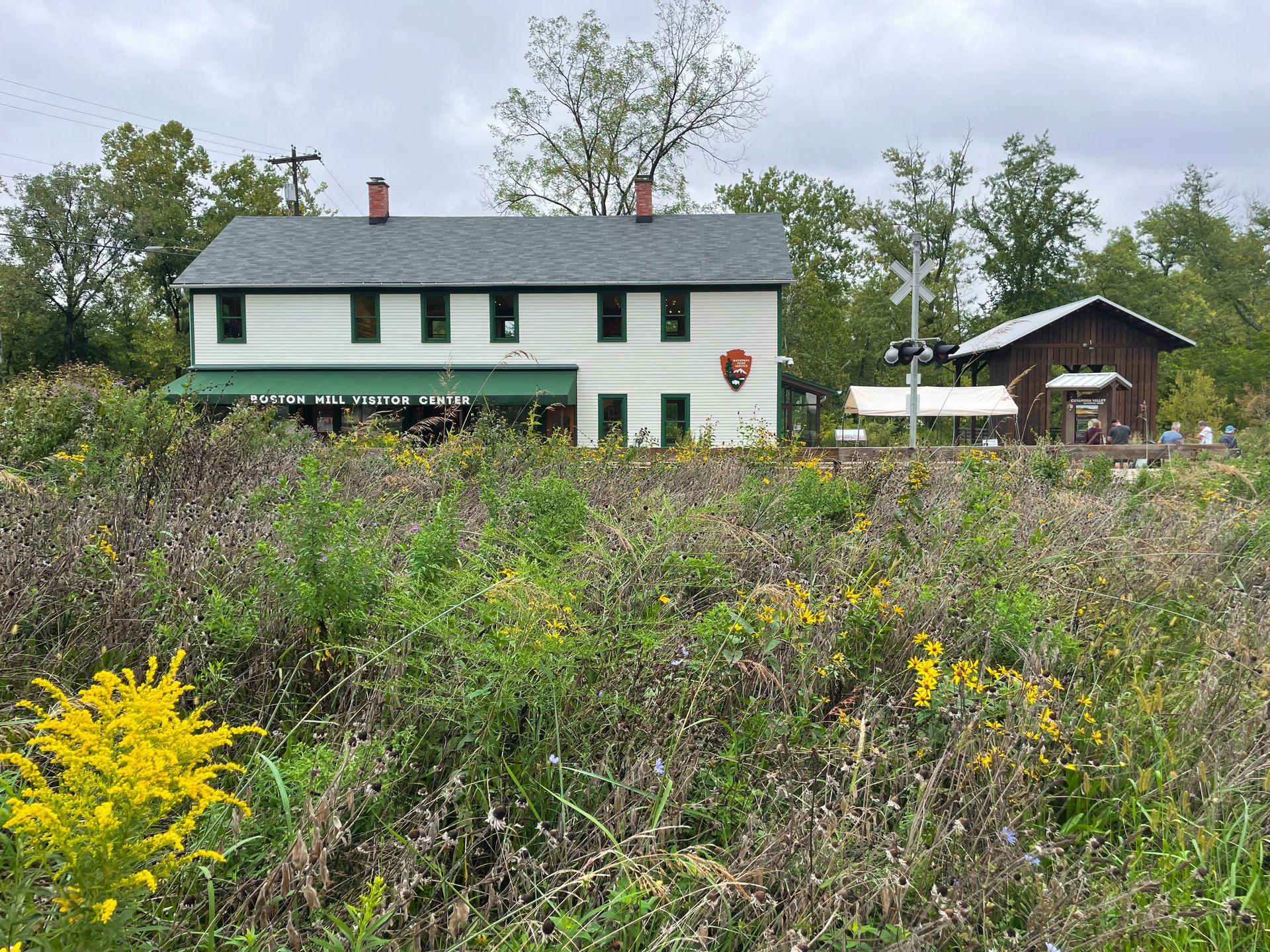 A photo of the front of the Boston Mill Visitor Center with green grasses and yellow flowers in front.