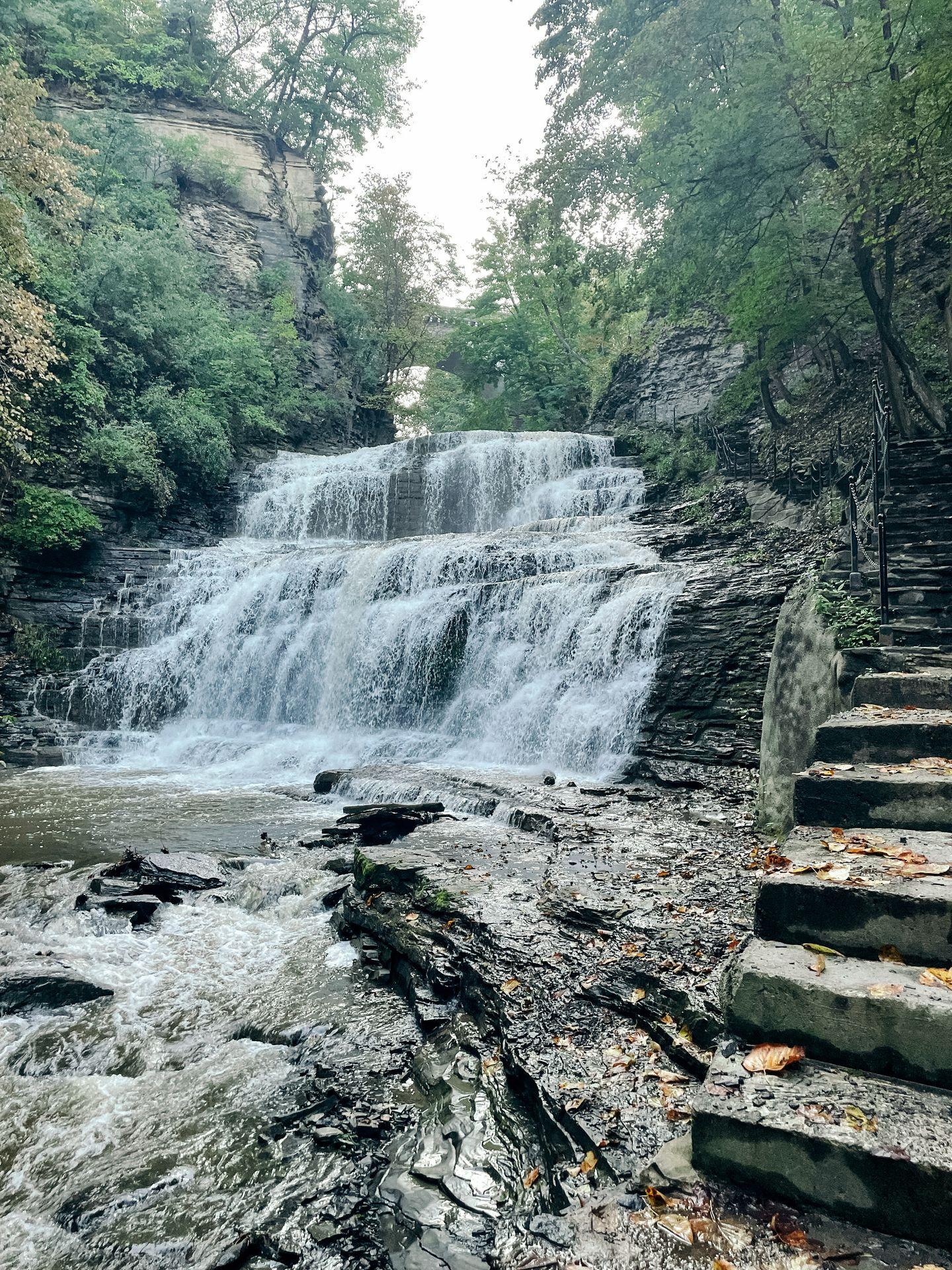A waterfall with stone steps climbing up next to it in Cascadilla Gorge.