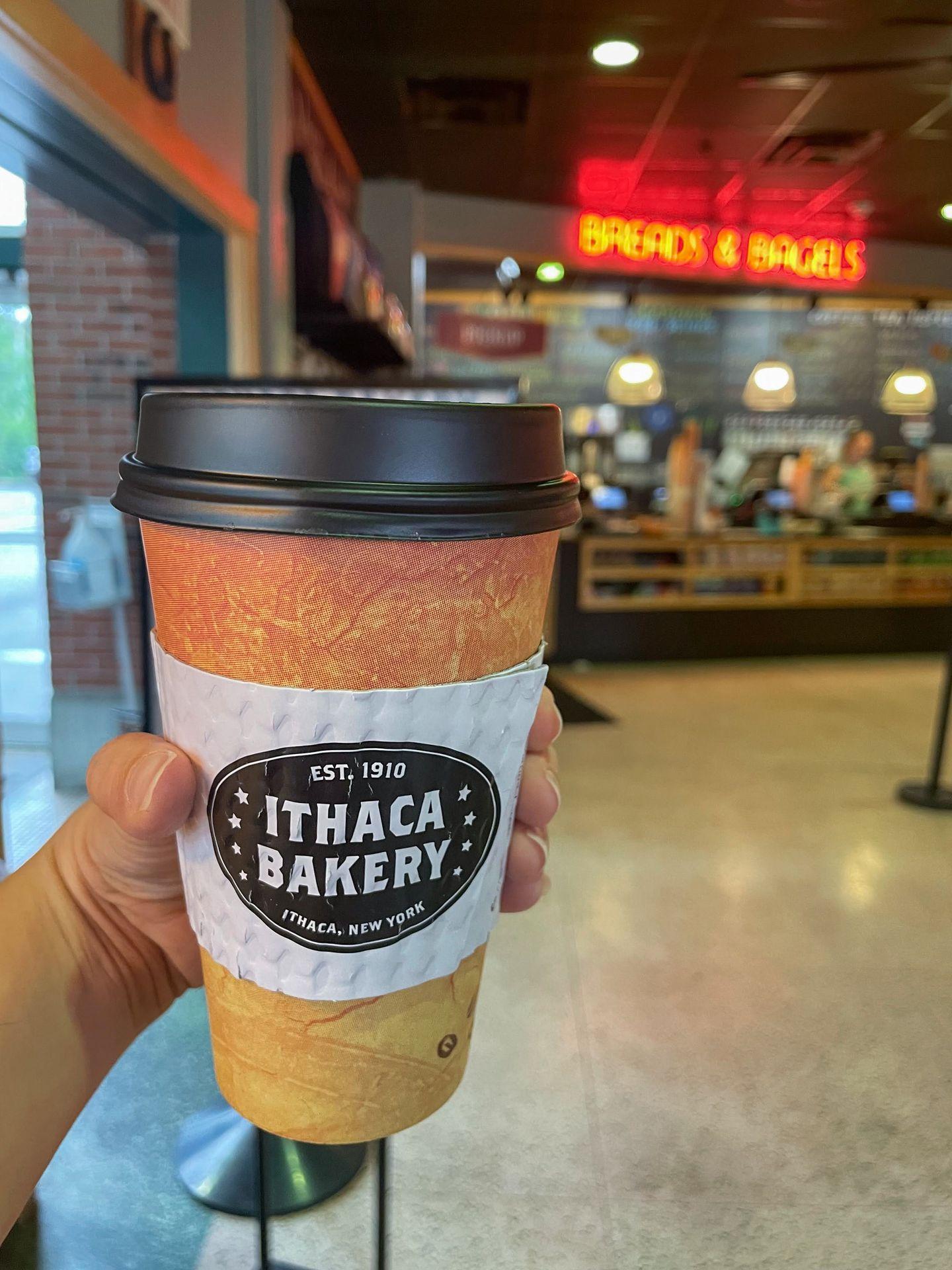 Holding up a to-go coffee from Ithaca Bakery.