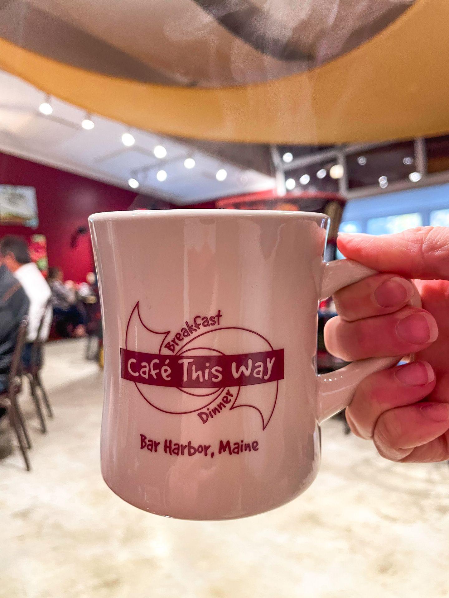 Holding up a mug that reads "Cafe This Way" inside the restaurant.