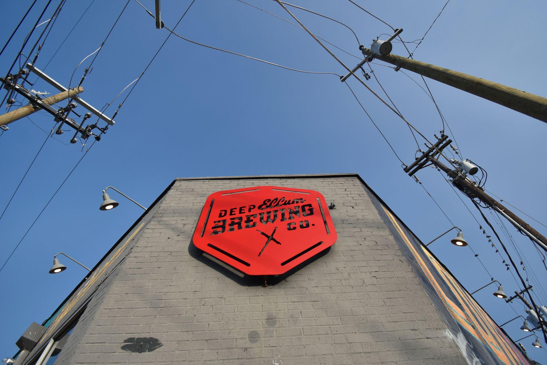Looking up at a red sign that reads "Deep Ellum Brewing Co" on a gray building