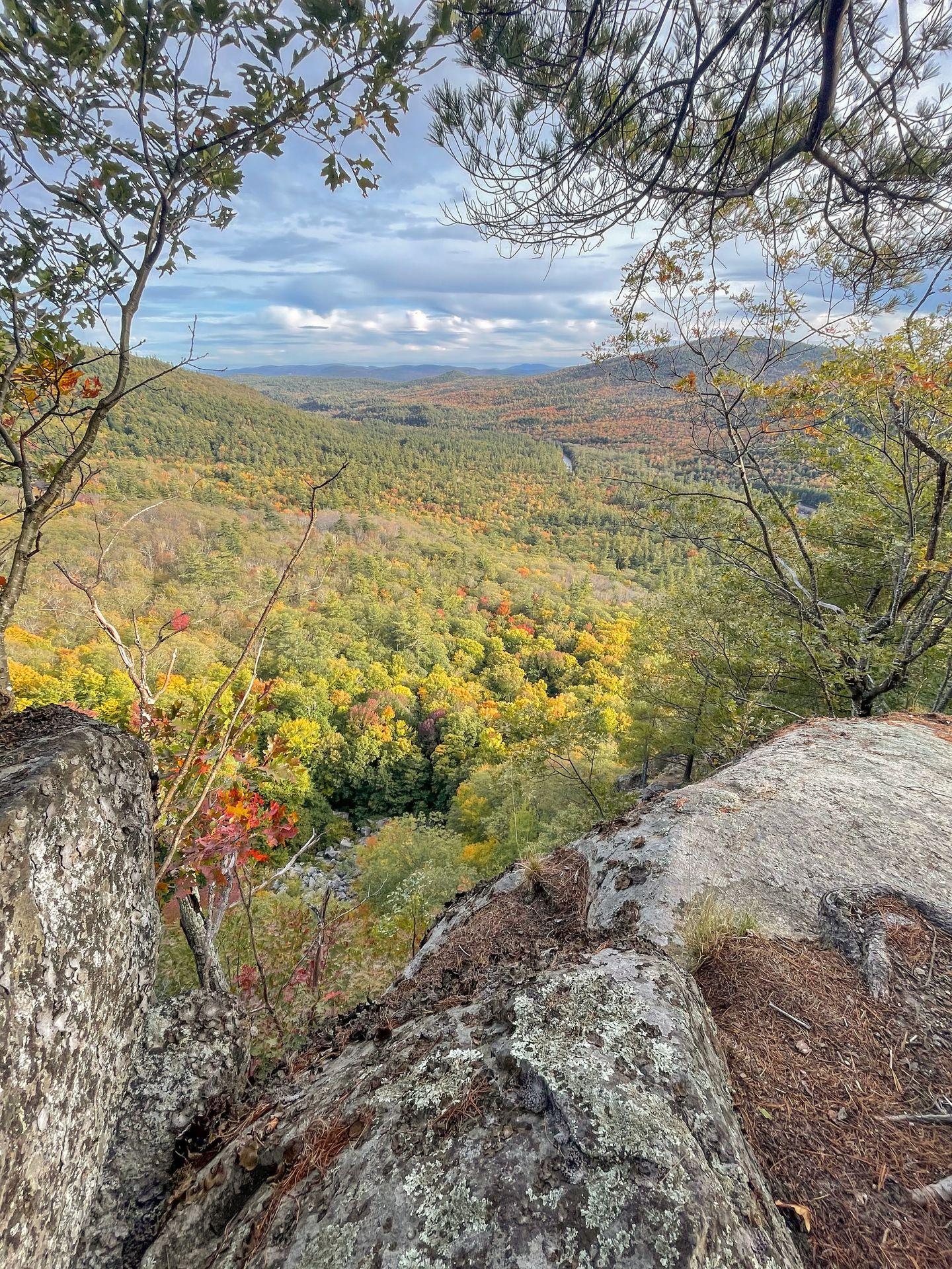 Looking through rocks and trees at a view of hills. There is some fall foliage in the distance.