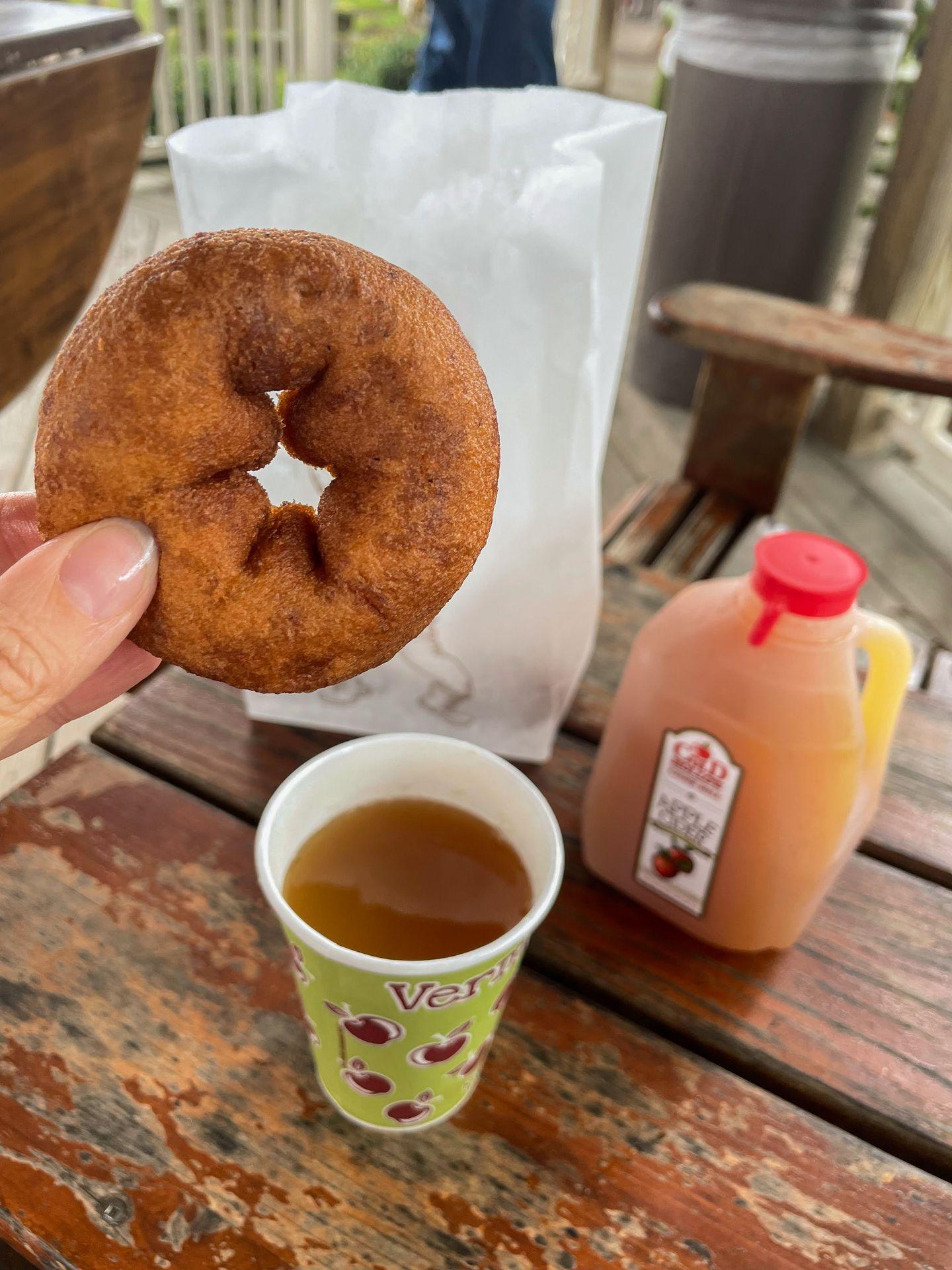 Holding up an apple cider donut next to a cup of hot apple cider.