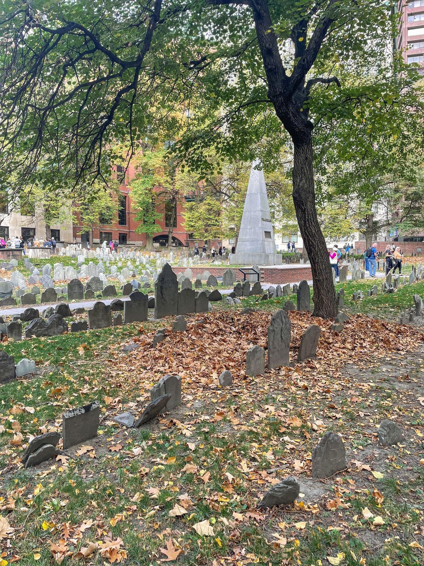 An historic cemetery with small, stone gravestones surrounded by fallen leaves.