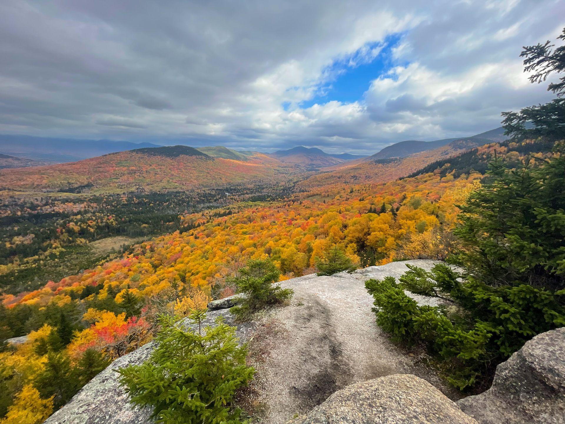 A beautiful view of mountains covered in fall foliage seen from North Sugar Peak in New Hampshire.